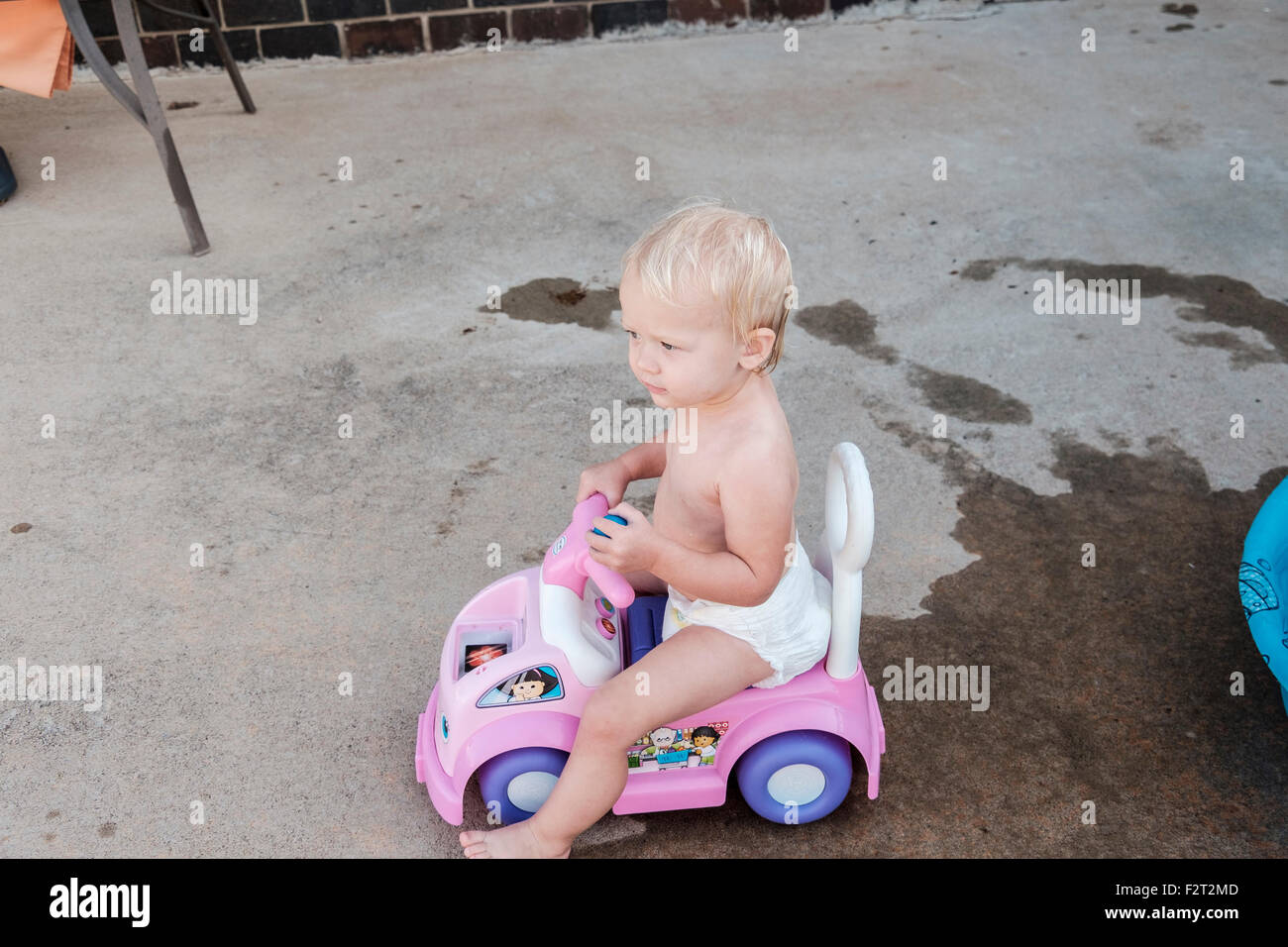 A one year old Caucasian baby girl plays with her riding toy car. Stock Photo