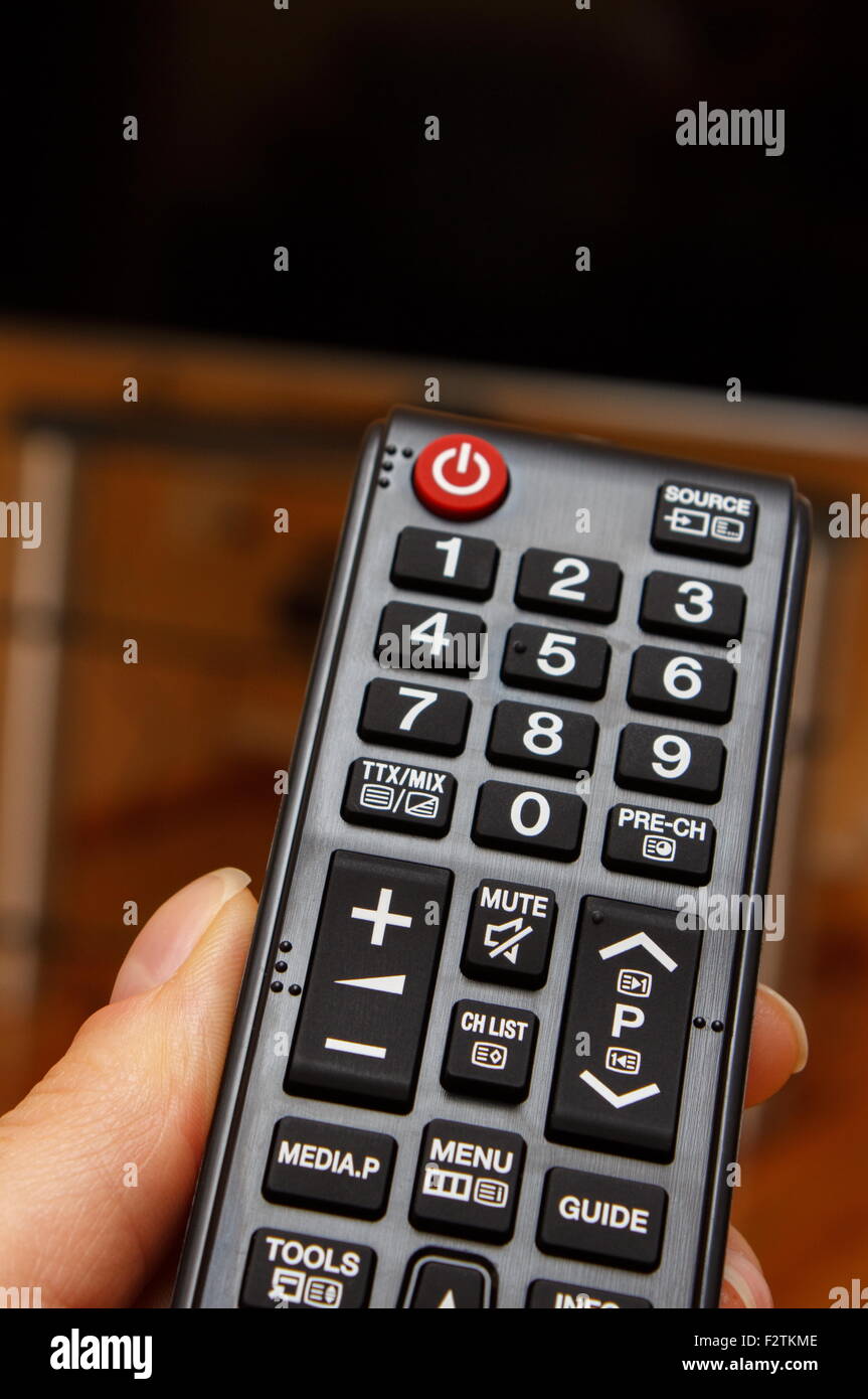 Hand holding infrared remote control for television and TV screen in background Stock Photo