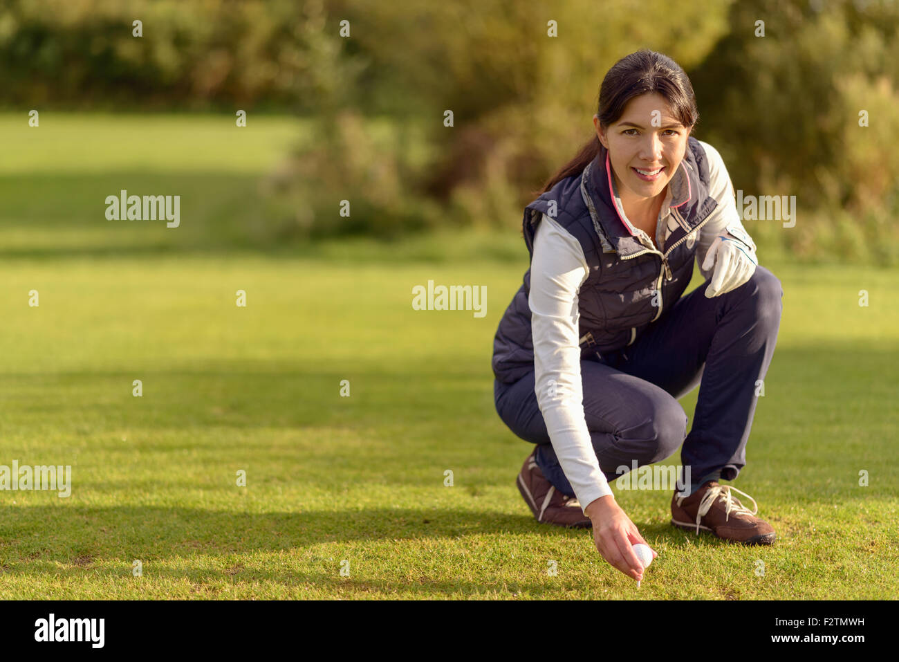 Smiling attractive young female golfer bending down on the fairway