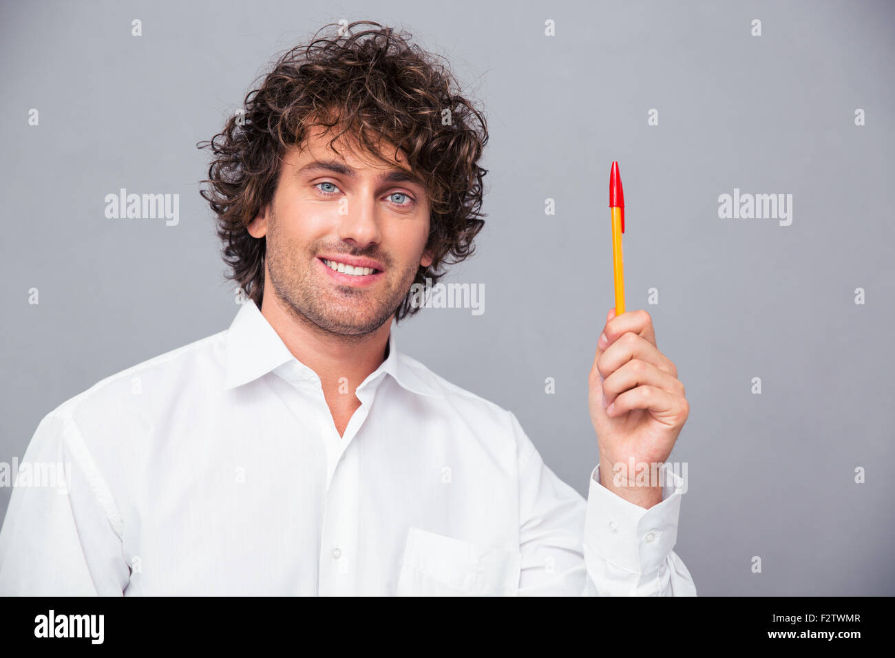 Portrait of a smiling businessman holding pen over gray background ...