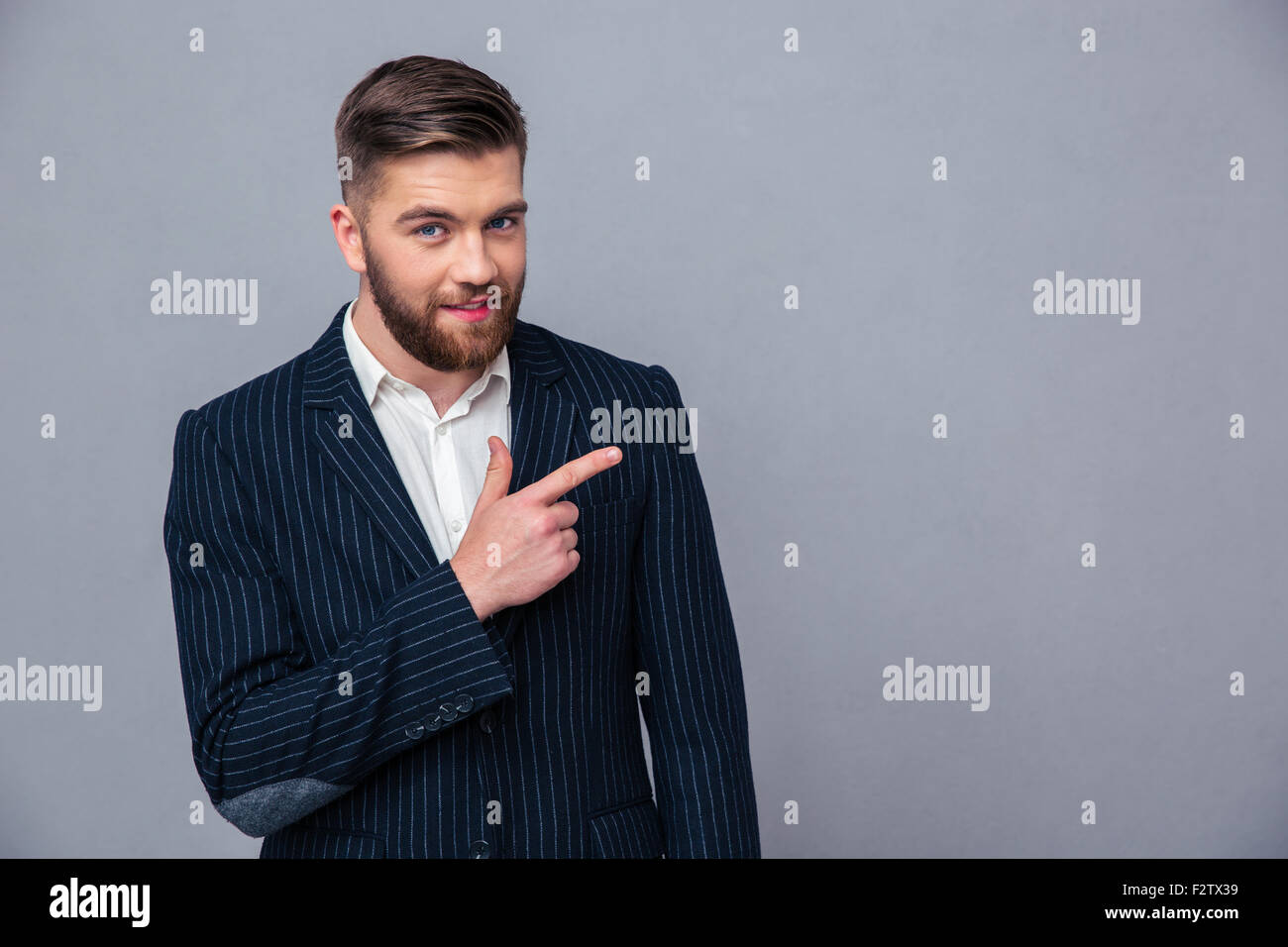 Portrait of a happy businessman pointing finger away over gray background Stock Photo