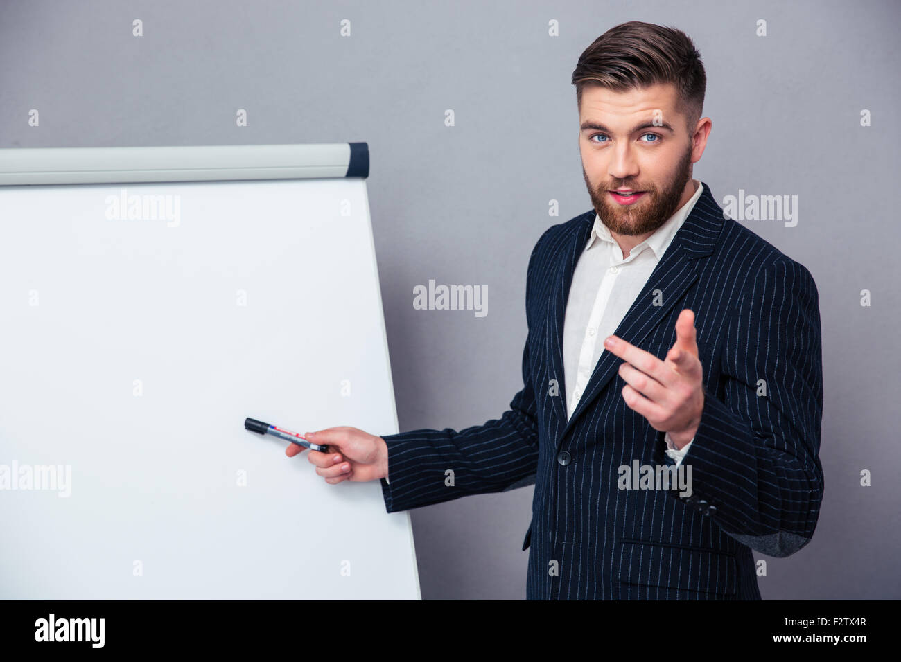 Portrait of a young businessman in suit presenting something on blank board over gray background Stock Photo