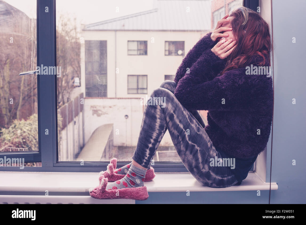 Sad young woman is sitting by the window Stock Photo