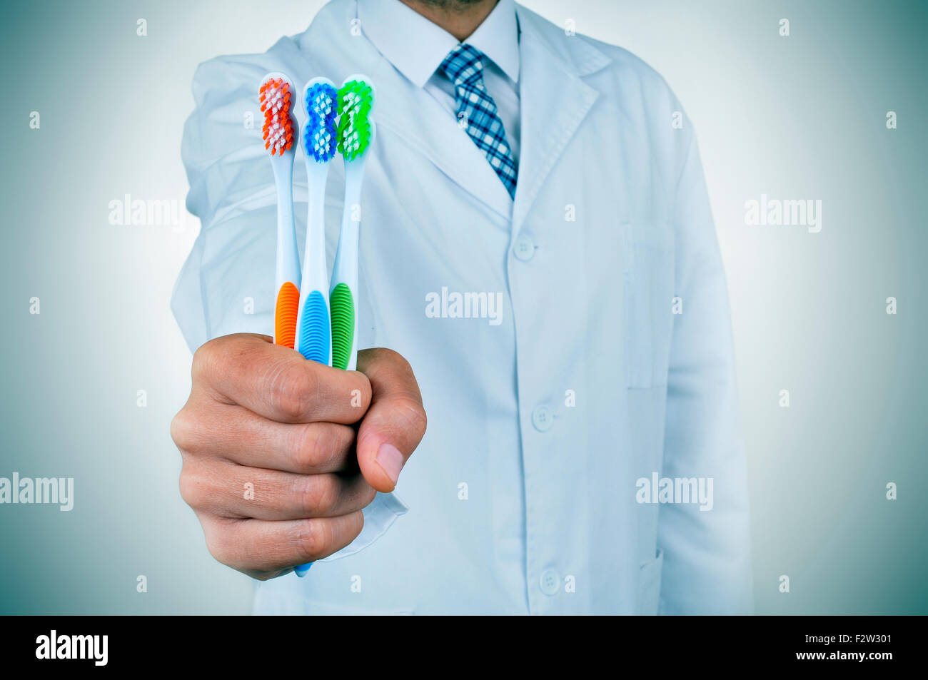 a young dentist man showing some toothbrushes depicting the importance of tooth brushing for a good oral hygiene Stock Photo