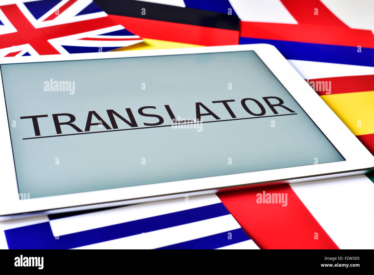 the word translator in the screen of a tablet computer surrounded by flags of different countries Stock Photo
