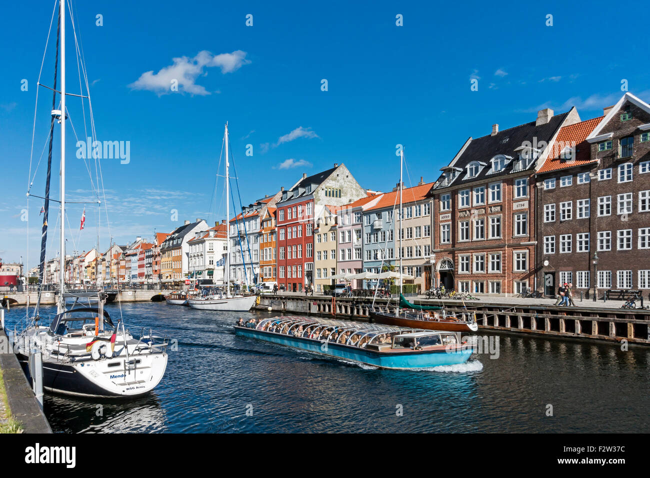 Colourful Nyhavn in Copenhagen Denmark with a packed canal touring boat leaving for a tour round the harbour Stock Photo