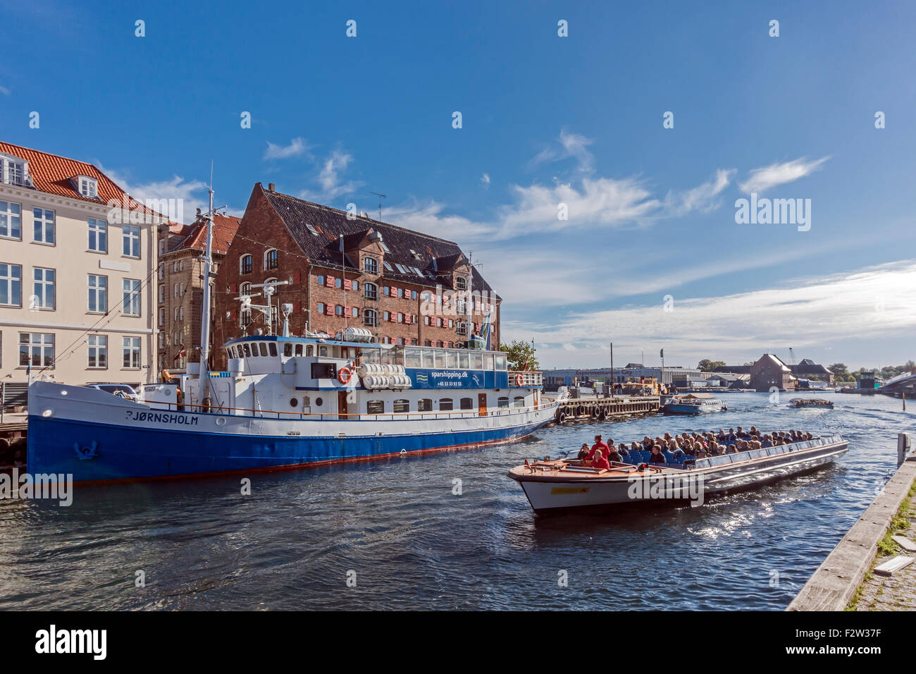 Colourful Nyhavn in Copenhagen Denmark with canal touring boat arriving back to Nyhavn after a tour round the harbour Stock Photo
