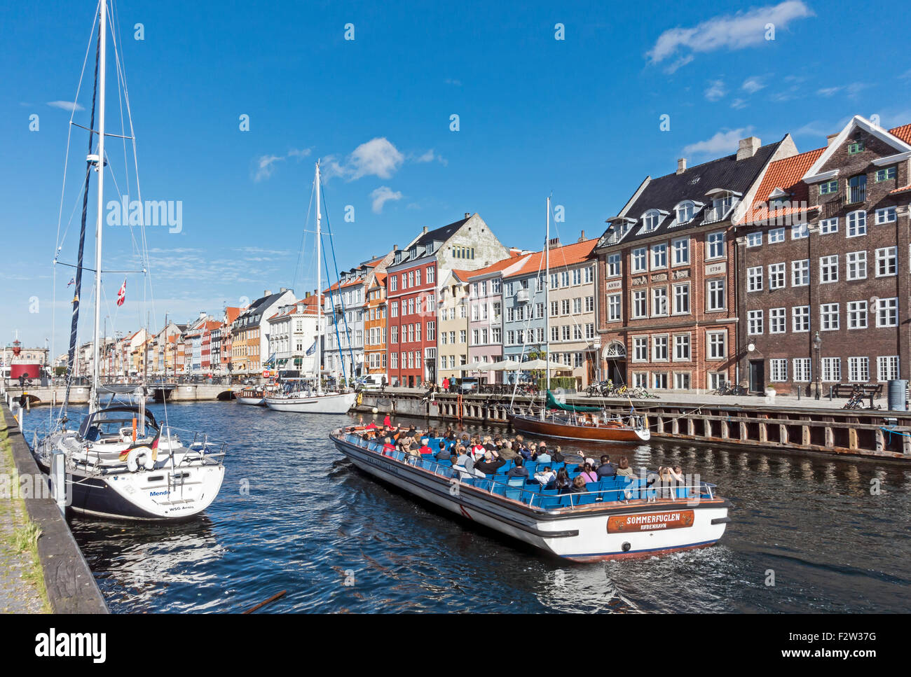 Colourful Nyhavn in Copenhagen Denmark with canal touring boat Sommerfuglen arriving back after a tour round the harbour Stock Photo