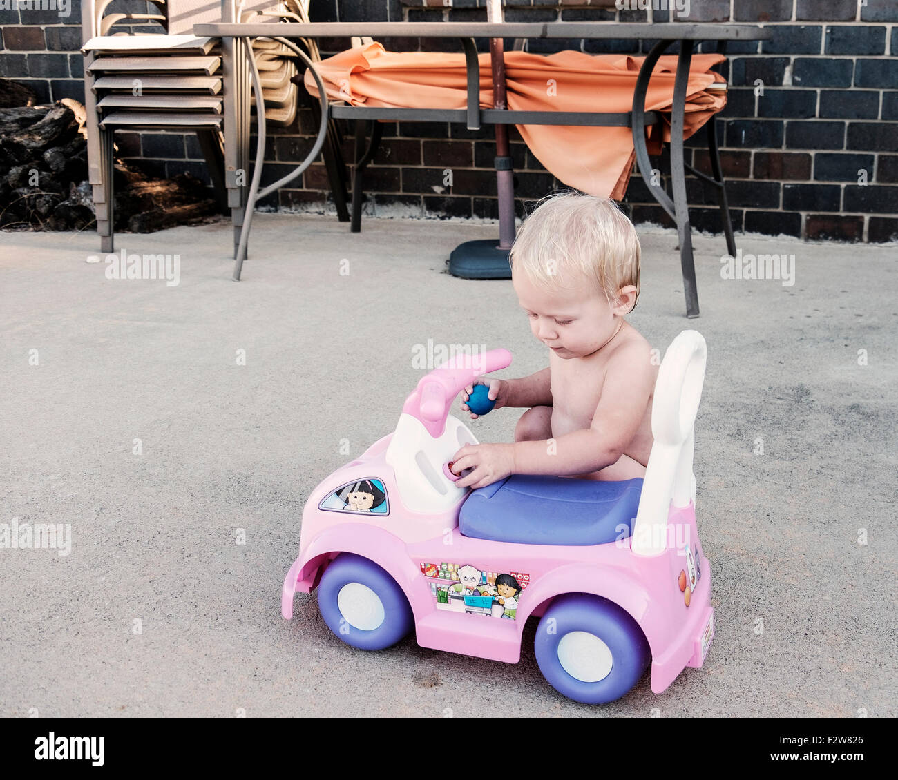 A one year old Caucasian baby girl plays with her pink vinyl riding toy car. USA Stock Photo