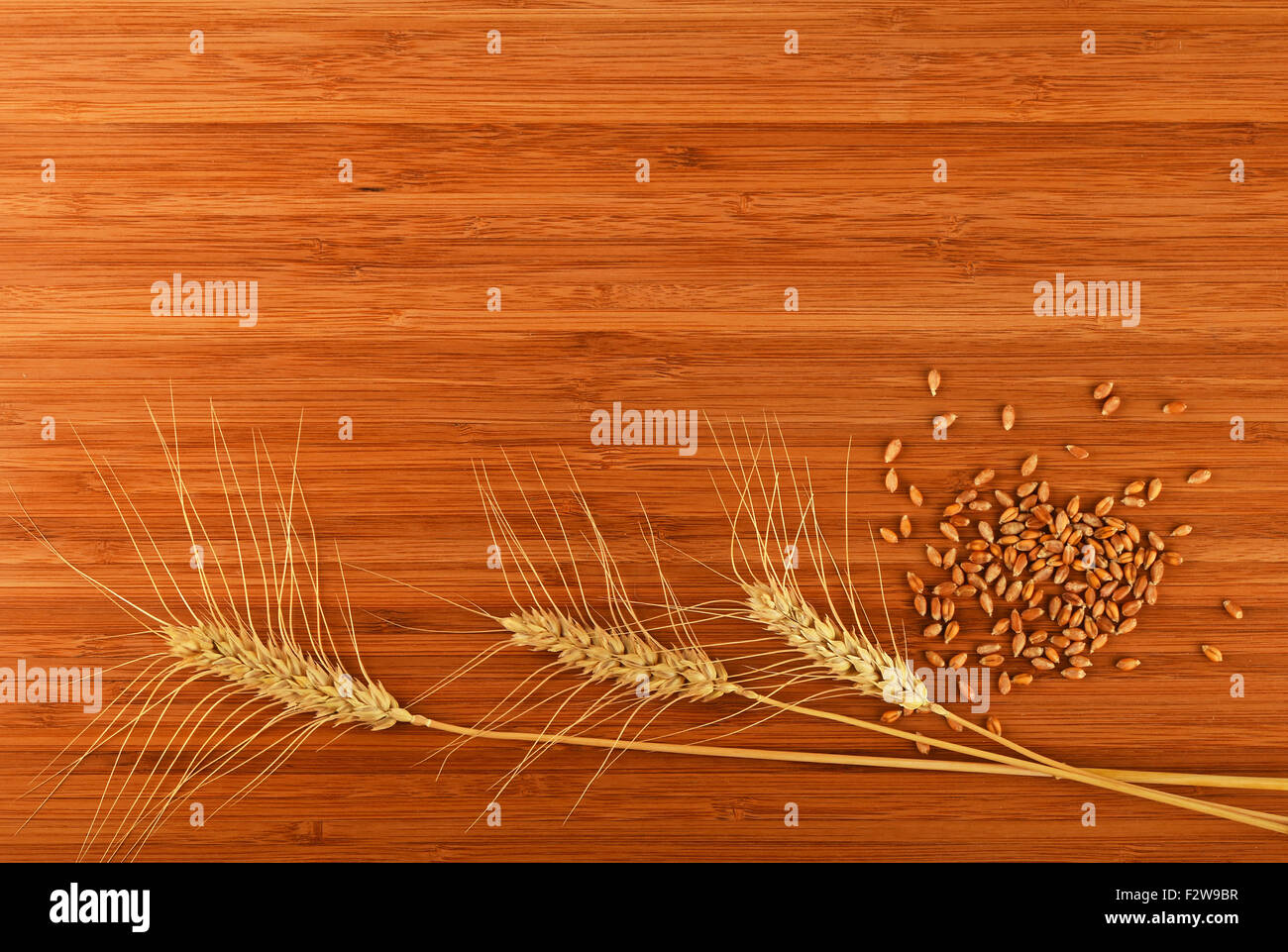 Wooden bamboo cutting board with three wheat ears and handful of ripe grains, add your text Stock Photo