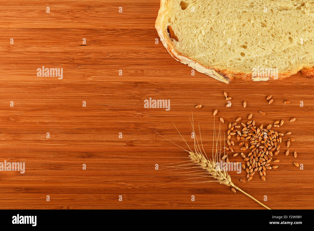 Wooden bamboo cutting board with one wheat ear, handful of ripe grains and a slice of bread - add your text Stock Photo