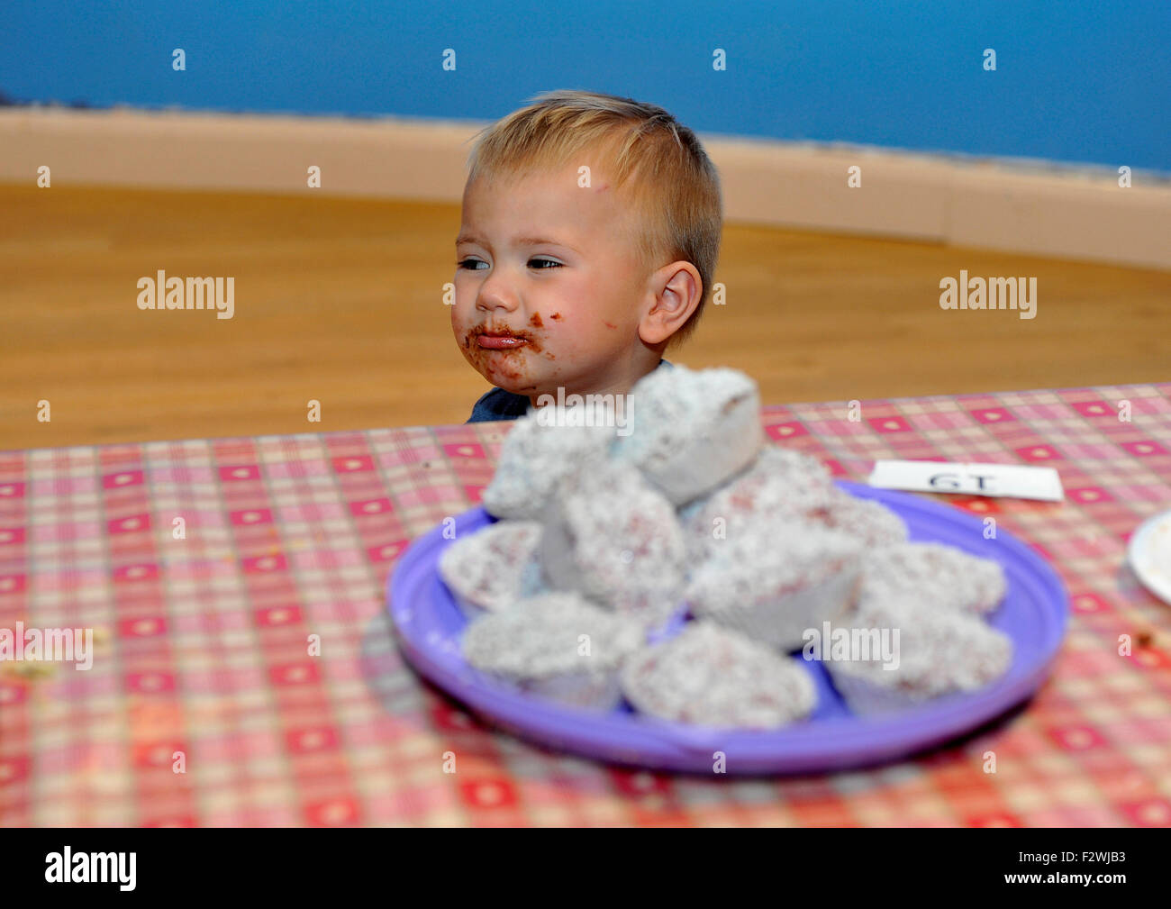 Young Irish boy with chocolate on his face passing a plate of cakes. Stock Photo