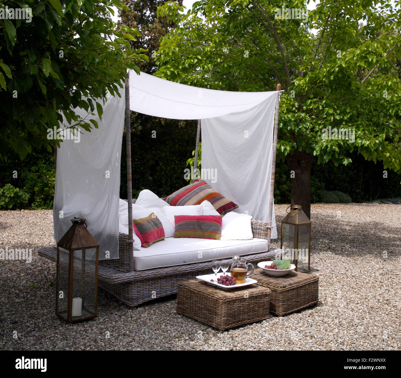 White and patterned cushions on day bed below white canopy in Italian country garden with wicker stools Stock Photo