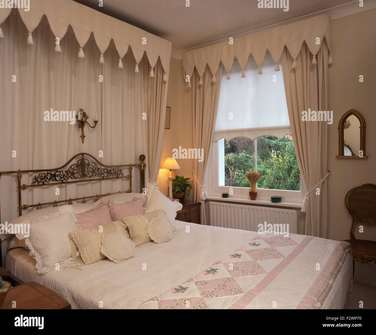 Gothic style canopy and drapes above brass bed in townhouse bedroom with cream curtains and pelmet Stock Photo