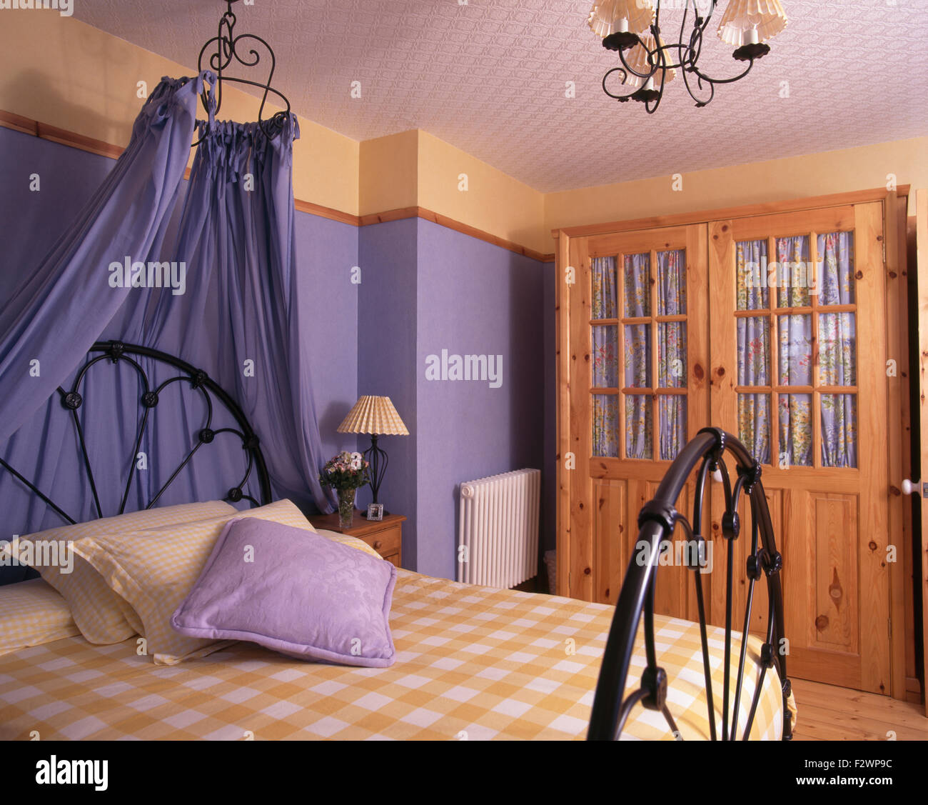 Coronet with blue drapes above wrought iron bed in nineties bedroom with pine wardrobe Stock Photo