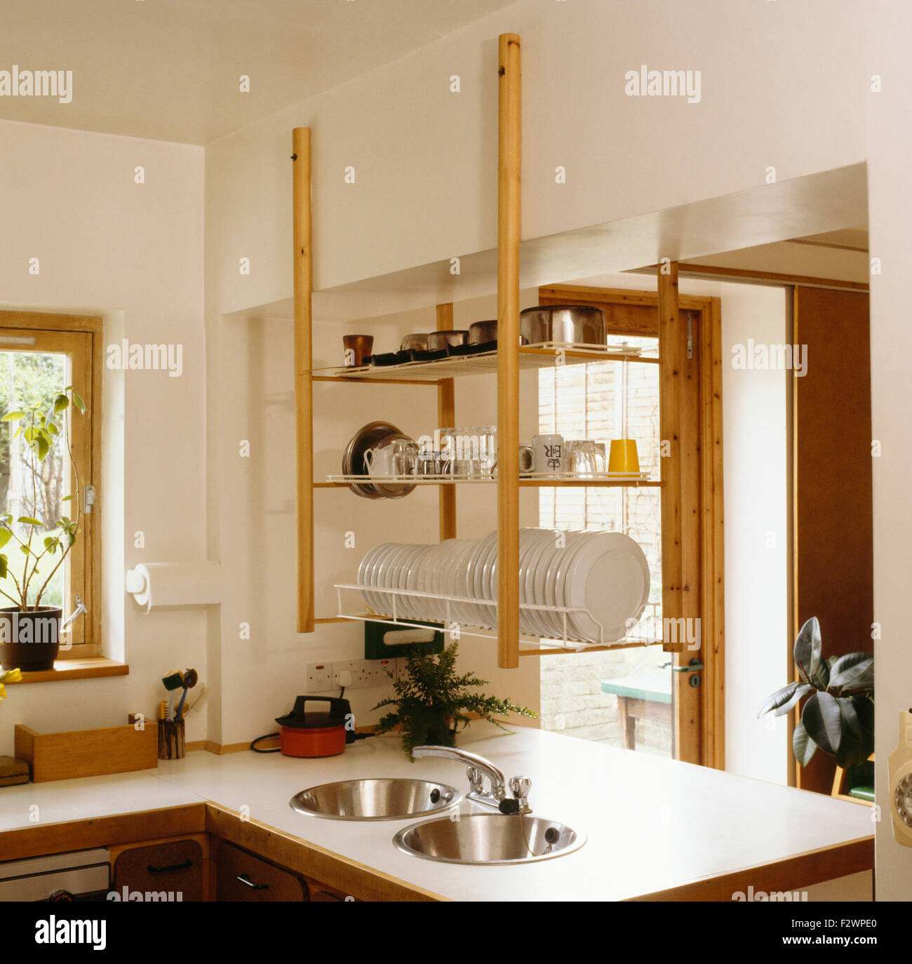 Open hanging shelves above fitted unit with stainless steel sinks in nineties kitchen Stock Photo