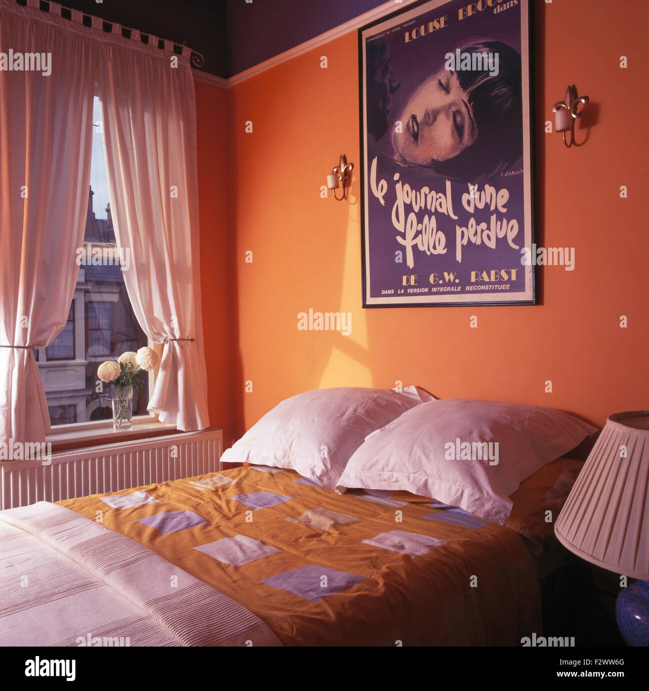 French film poster above bed in orange nineties bedroom with white drapes on the window Stock Photo