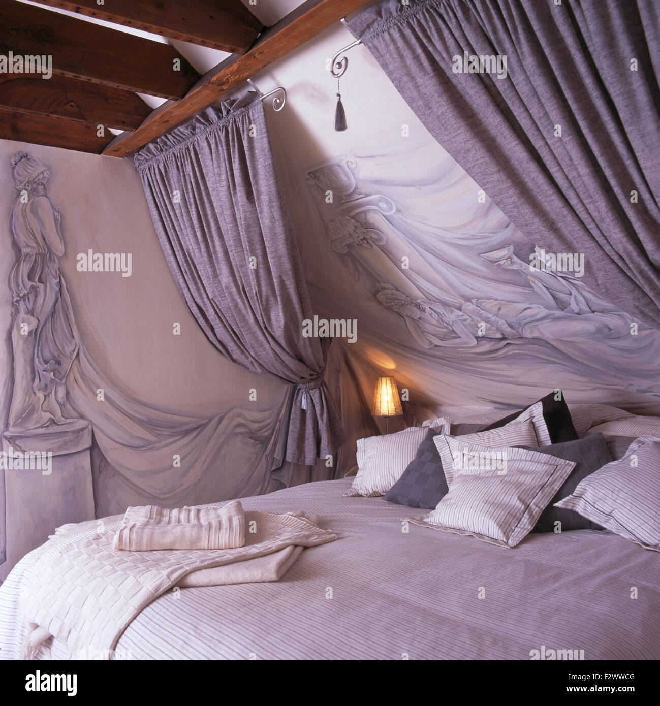 Trompe-l'oeil classical statues on wall and sloping ceiling in nineties attic bedroom with grey drapes above bed Stock Photo