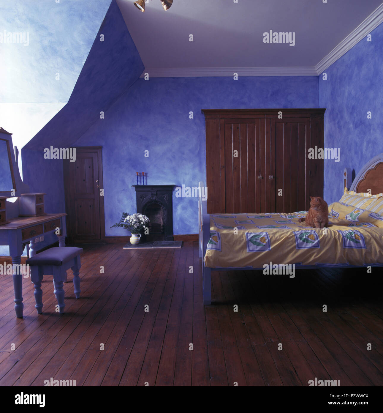 Wooden flooring in large blue country bedroom with walls painted in a sponging effect Stock Photo