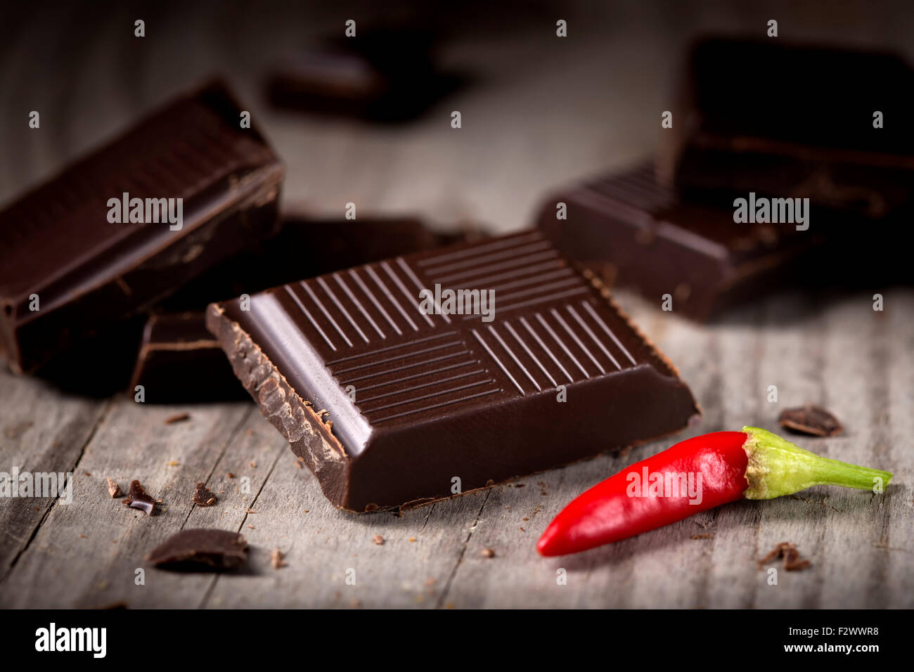 Chopped Chocolate with Red Chilli Pepper on wooden background closeup. Chunks of Broken dark chocolate bar on wood table macro. Stock Photo