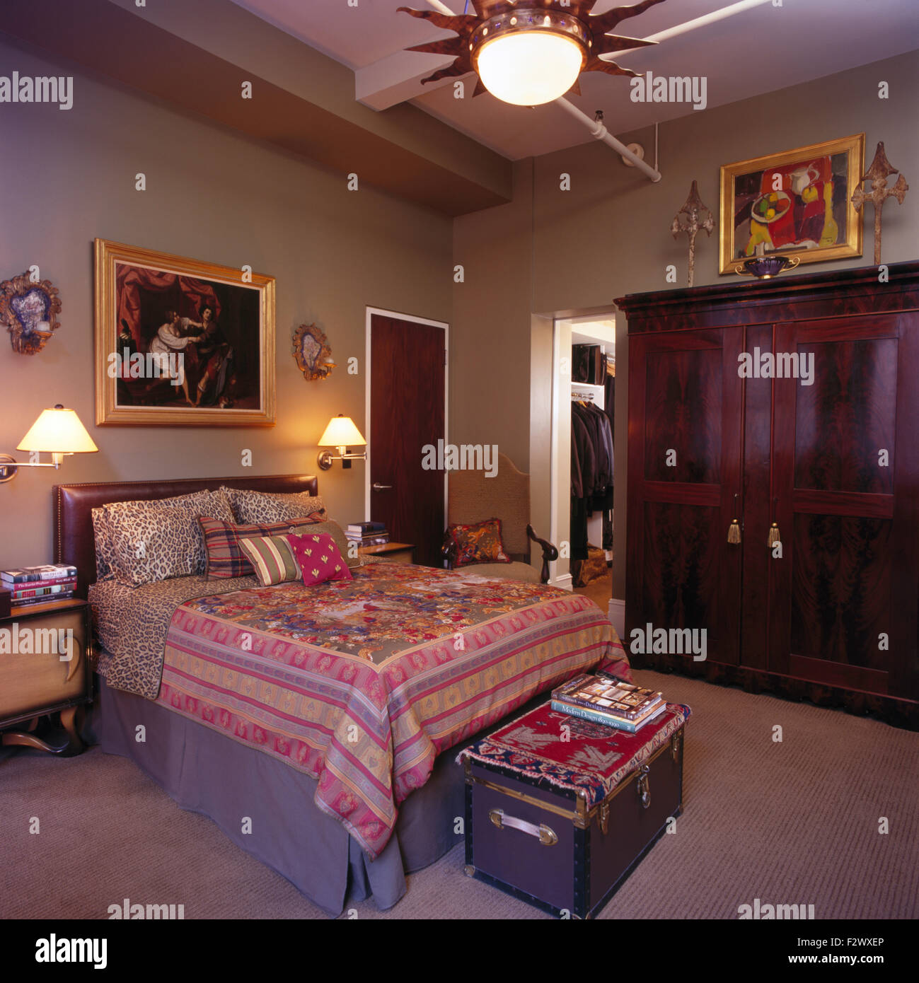 Leopard-print linen and an Indian bedspread on bed in brown nineties bedroom with a mahogany wardrobe Stock Photo