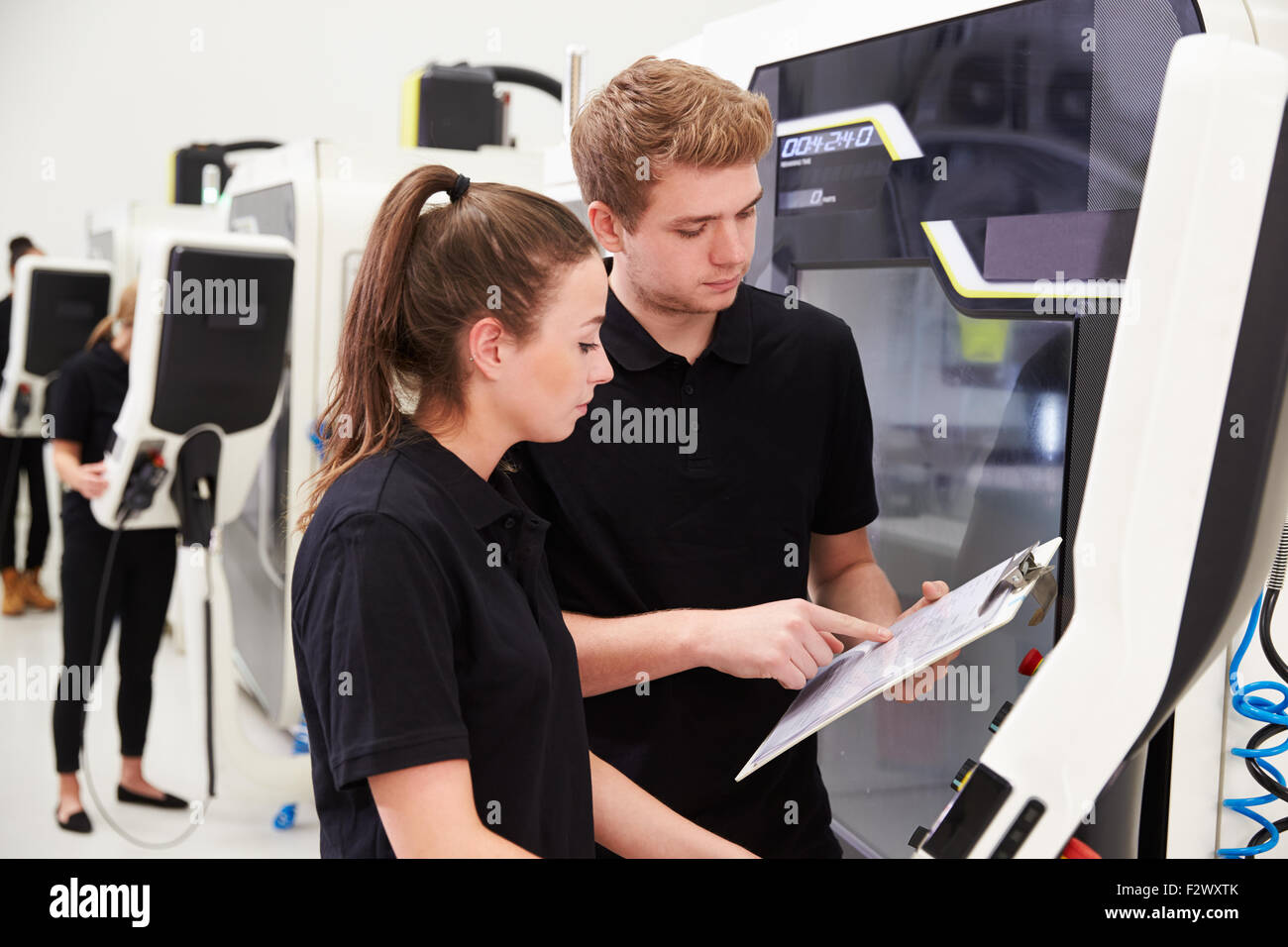 Two Young Engineers Operating CNC Machinery On Factory Floor Stock ...