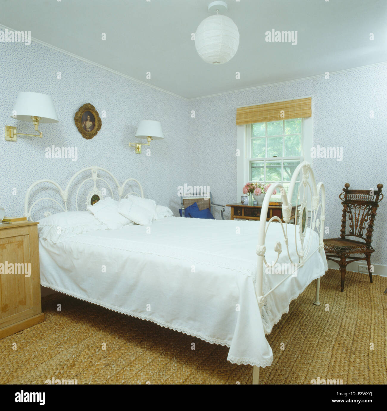 White wrought iron bed with white bedcover in bedroom with sisal carpet and pale blue