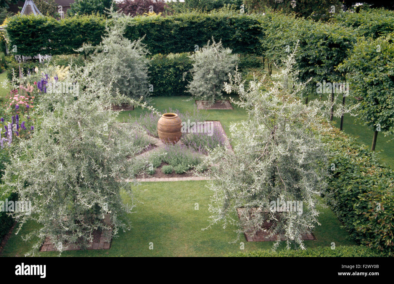 Weeping pear trees growing in corners of lawn with small central knot garden with a large pithoi pot Stock Photo