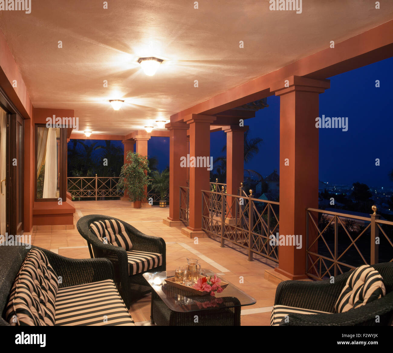 Striped cushions on black wicker chairs on veranda of large modern Spanish villa at night time Stock Photo