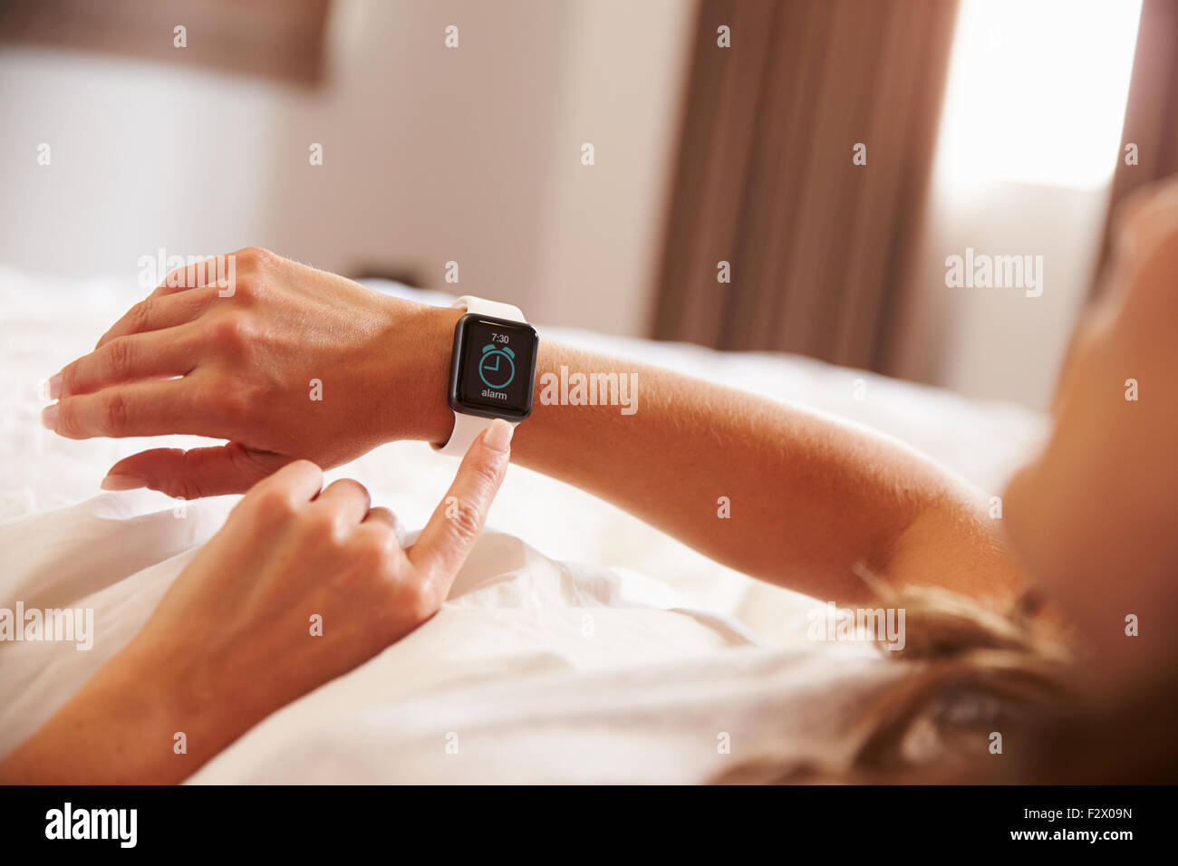 Woman Lying in Bed Woken Up by Alarm Clock App on Smart Watch Stock Photo