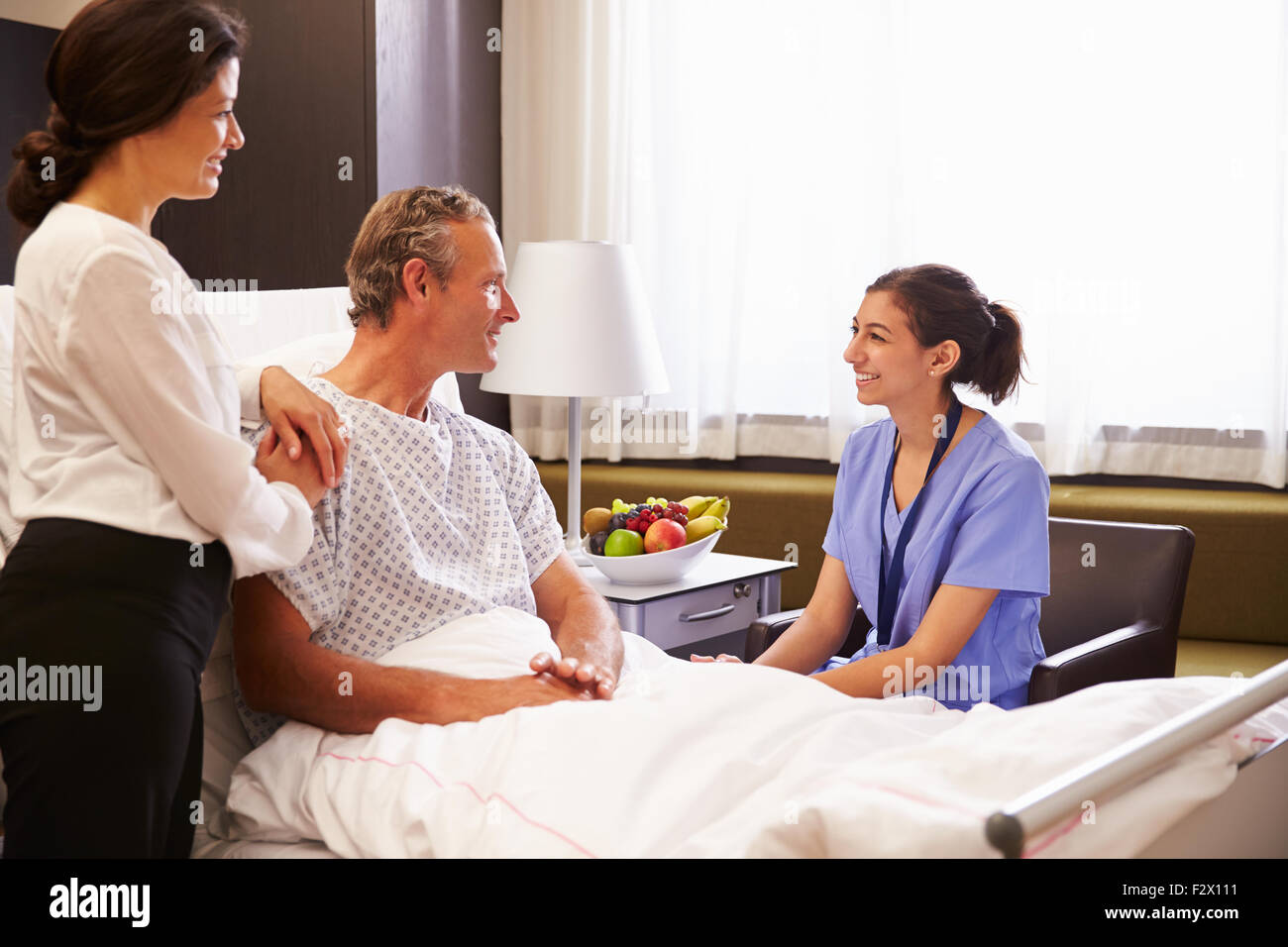 Nurse Talking To Male Patient And Wife In Hospital Bed Stock Photo - Alamy