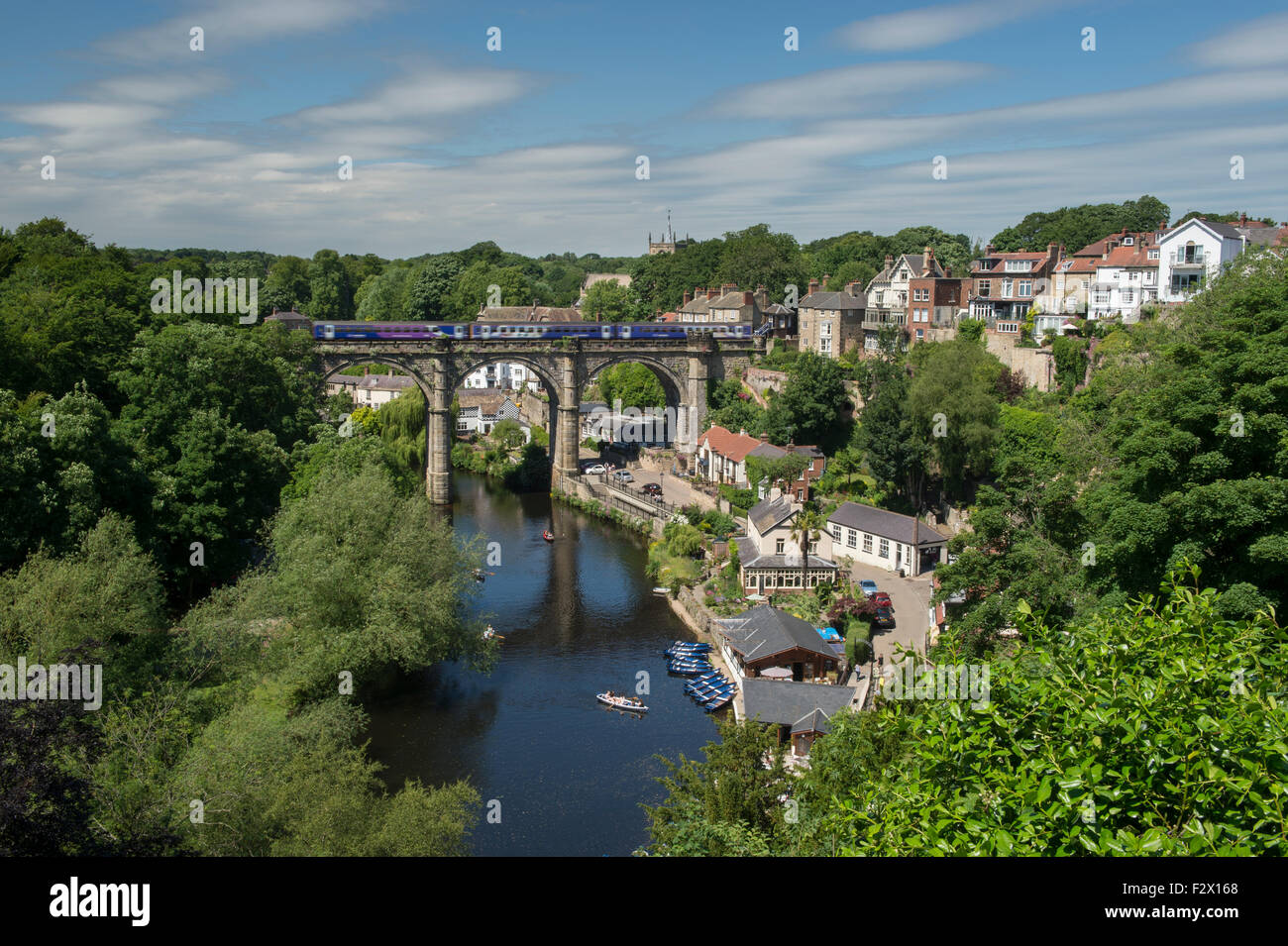 Scenic sunny summer Knaresborough (train on viaduct, boating on River Nidd, gorge, riverside & hillside buildings, blue sky) - Yorkshire, England, UK Stock Photo