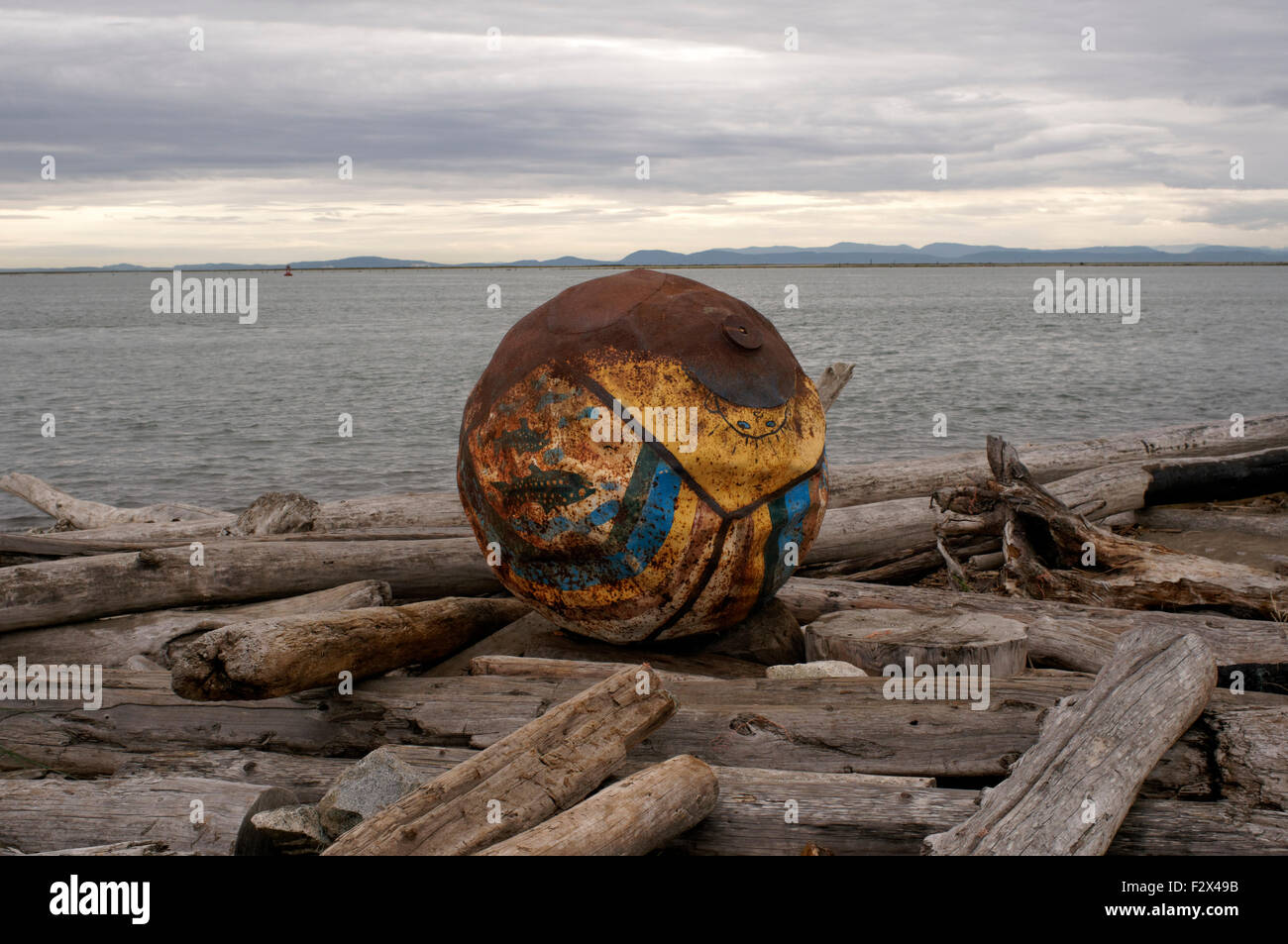 Colourful iron mooring buoy washed up on an isolated beach littered with driftwood logs, Garry Point, Steveston, Richmond, BC, Canada Stock Photo