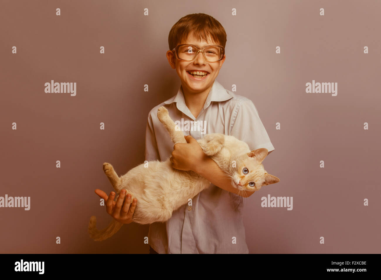 a boy of 10 years of European appearance with glasses holding a cat in hands on a gray background retro Stock Photo