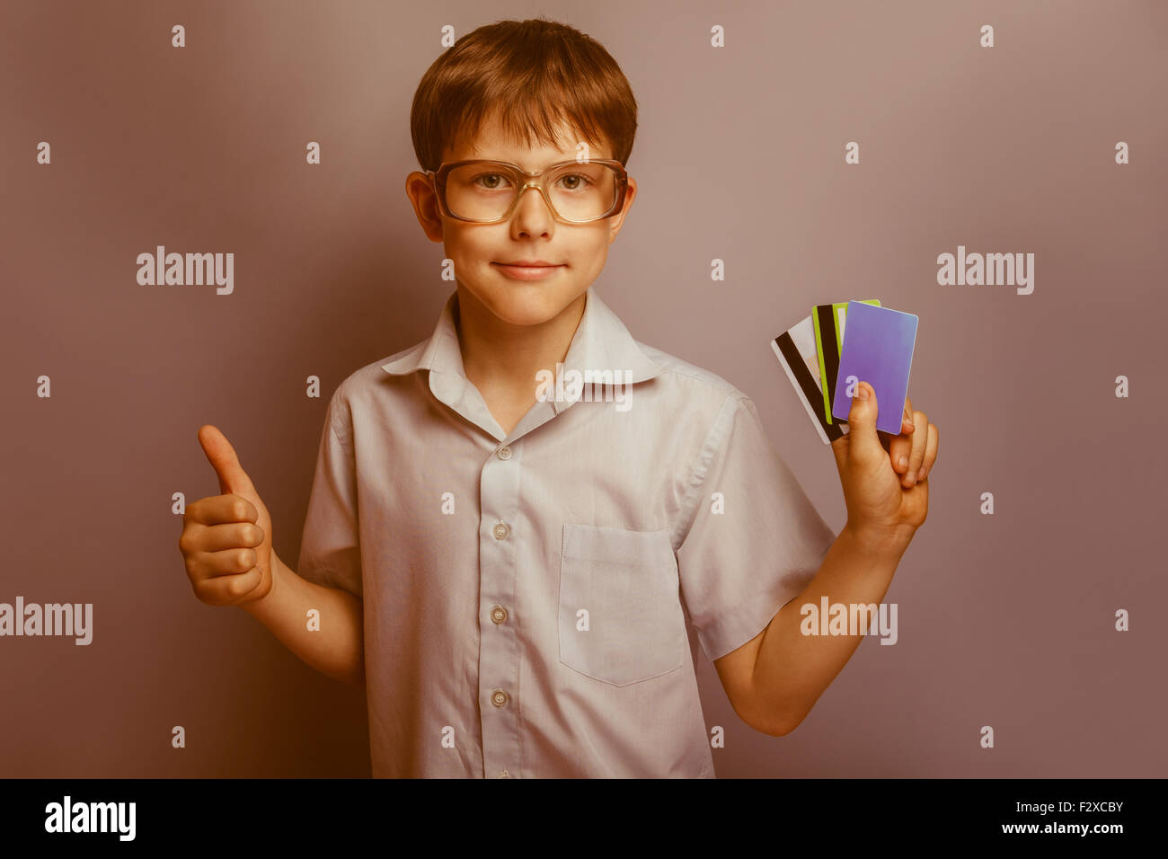 a boy of 10 years of European appearance with glasses holding kriditnye card in the hands of a thumbs up on a gray  background r Stock Photo