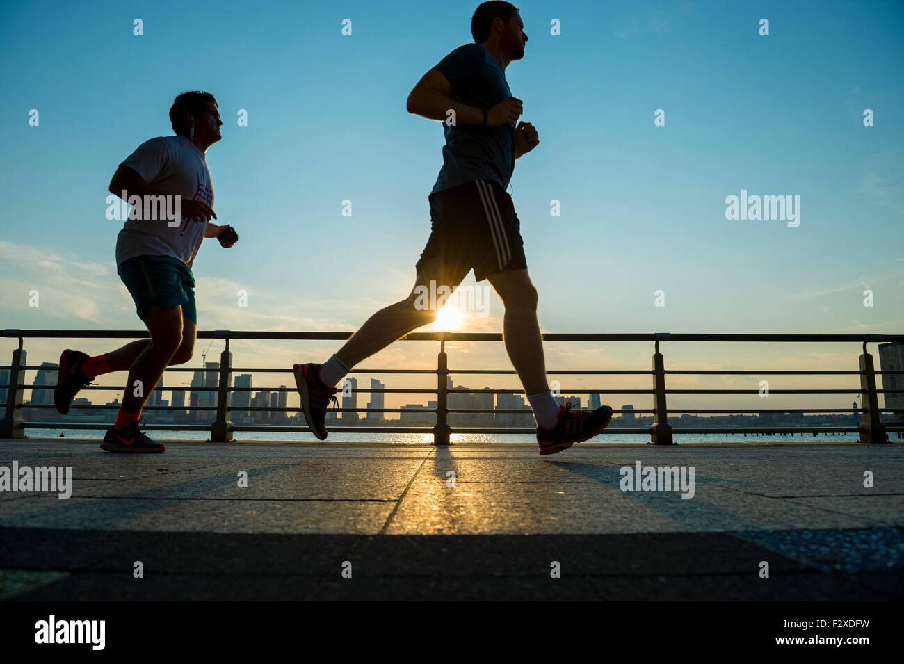 NEW YORK CITY, USA - AUGUST 15, 2015: Silhouettes of men run at sunset on the Hudson River boardwalk at sunset. Stock Photo