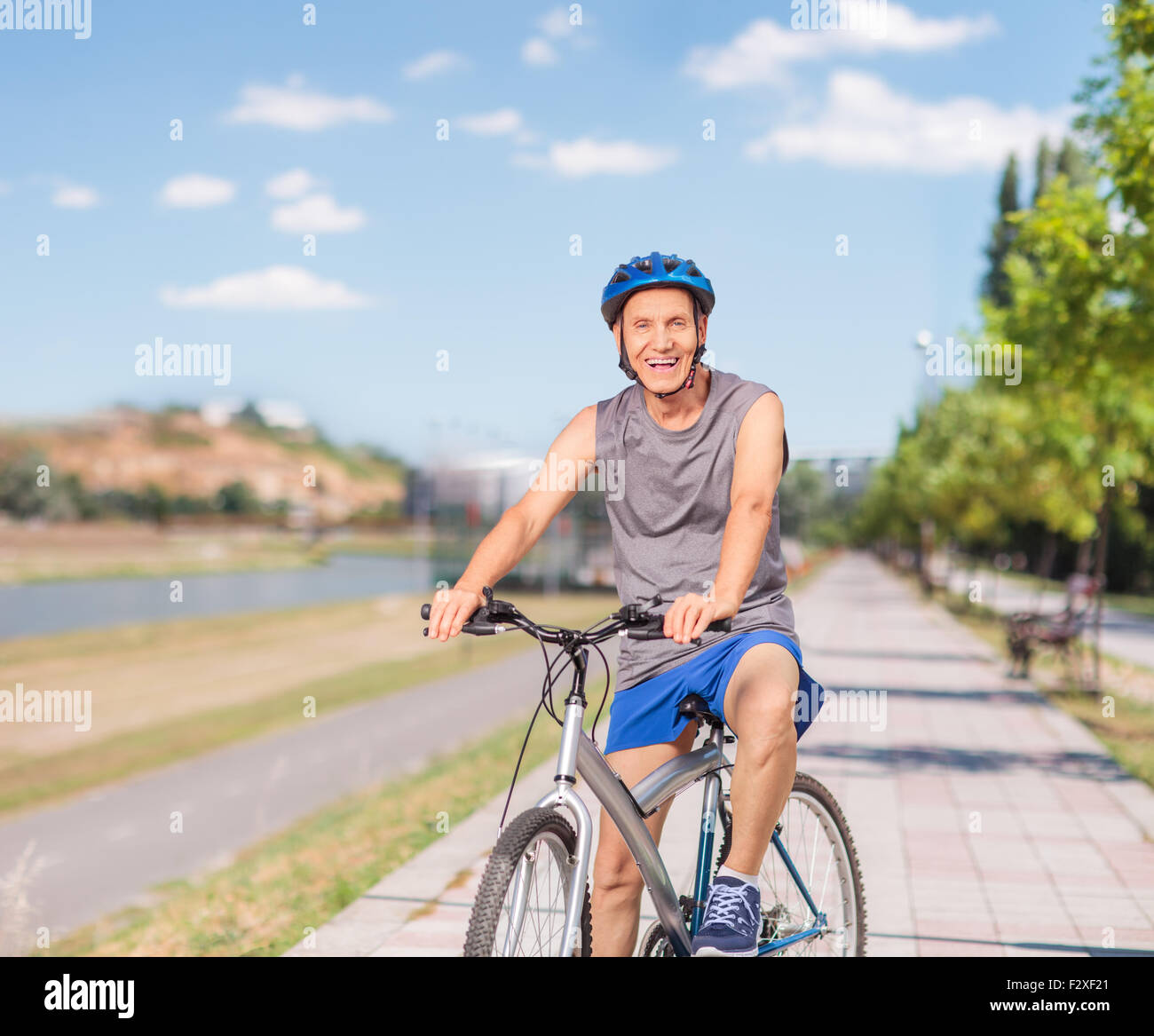 Cheerful senior man in sportswear posing with his bike on a sidewalk and looking at the camera shot with tilt and shift lens Stock Photo