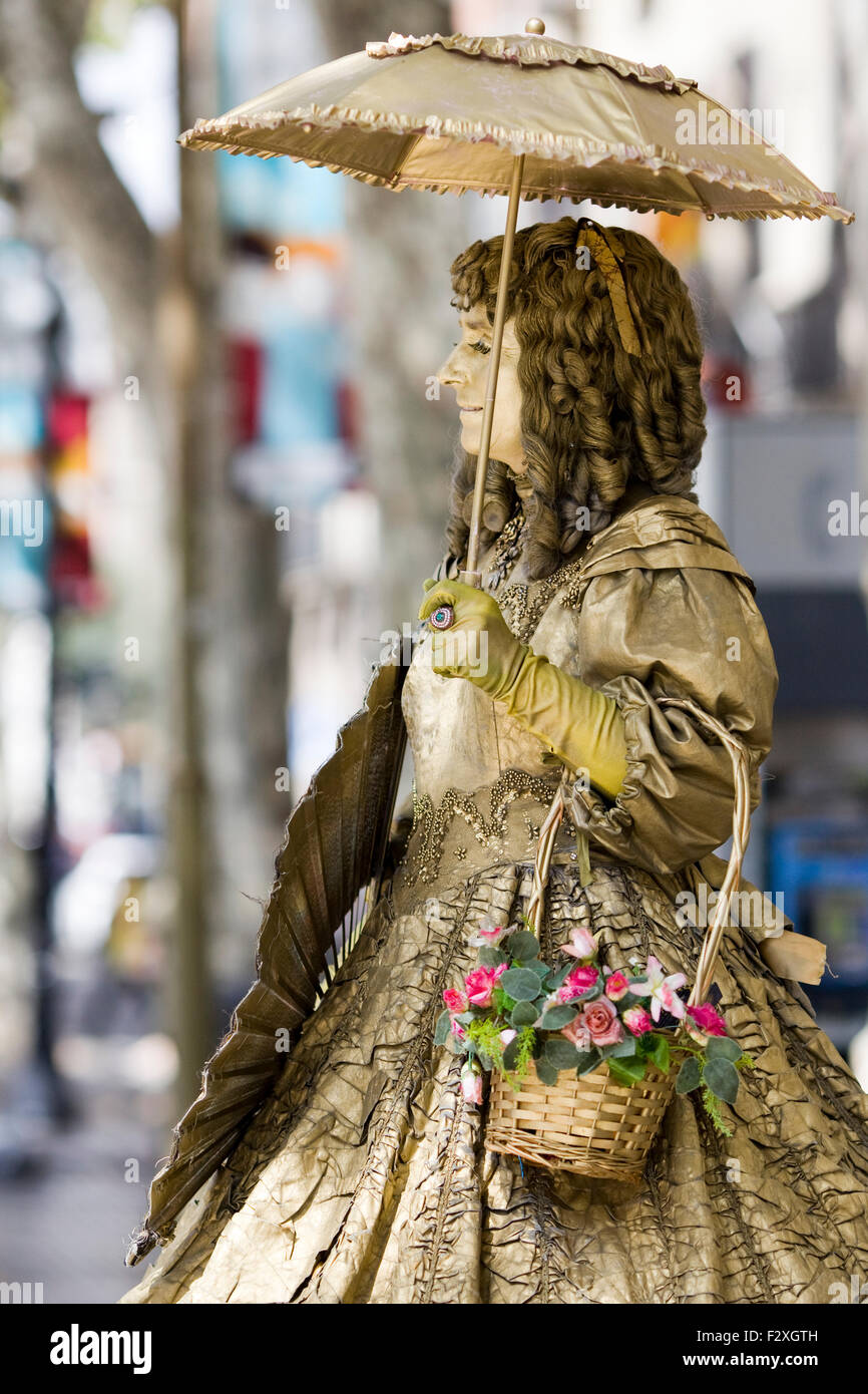 woman in gold with basket of flowers busking on the street of Barcelona Stock Photo
