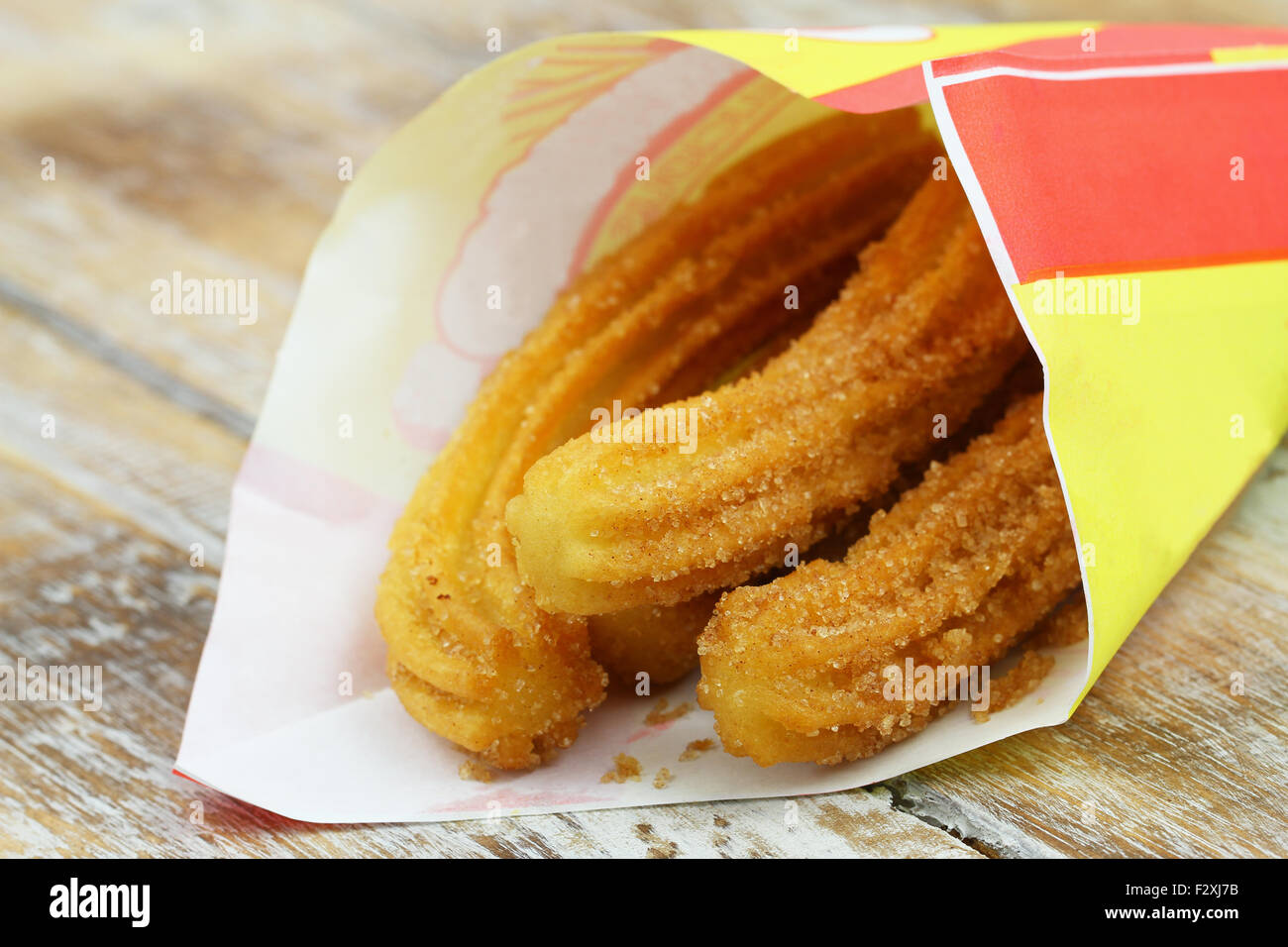 Spanish churros in paper bag on rustic wooden surface, closeup Stock Photo