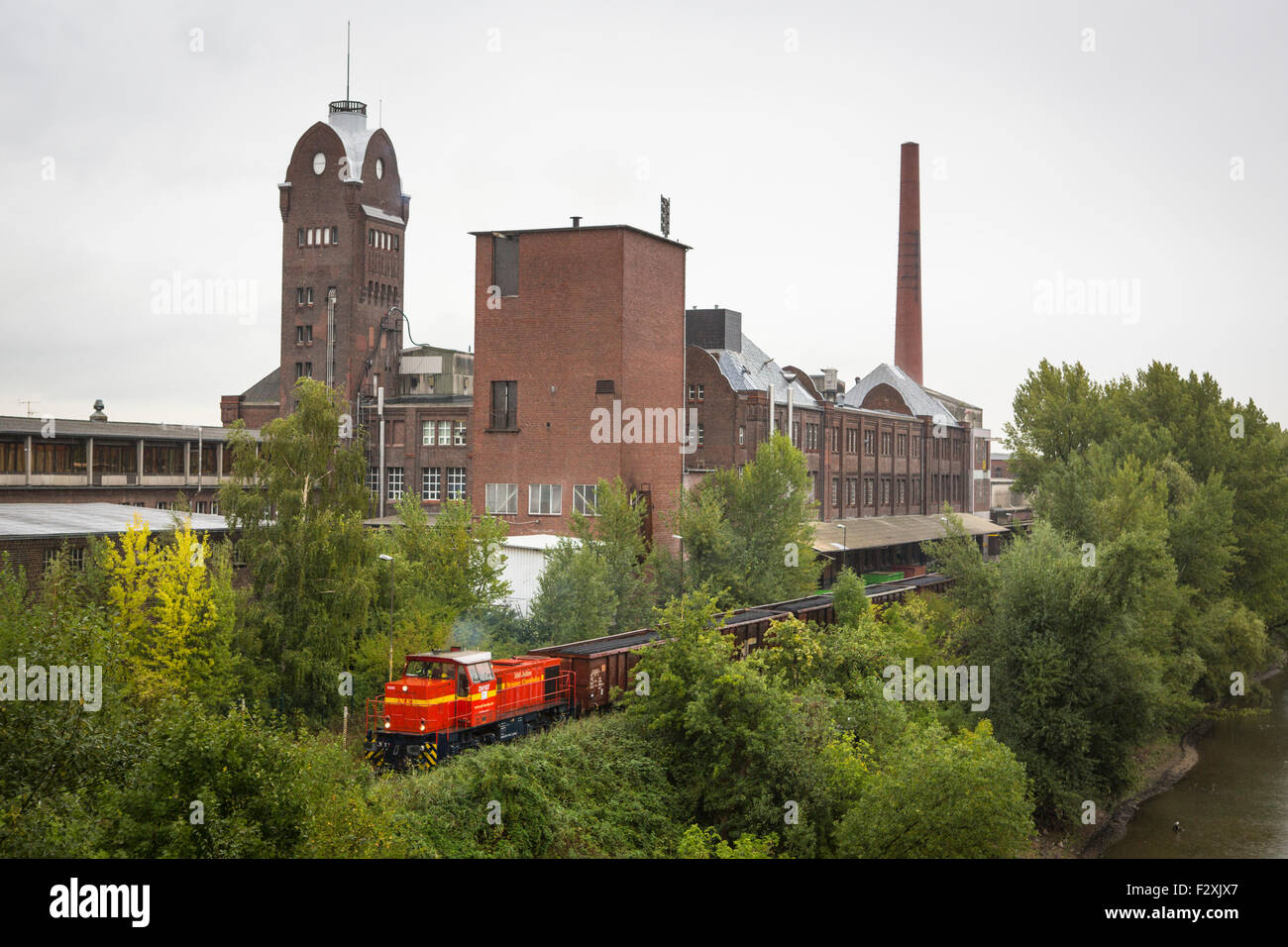 Train loaded with coal passing a factory in the industry park of Düsseldorf in the Ruhr infrastructure area in Germany Stock Photo