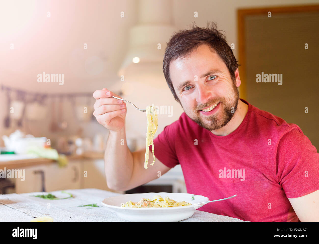 Young handsome man in the kitchen eating salmon tagliatelle Stock Photo