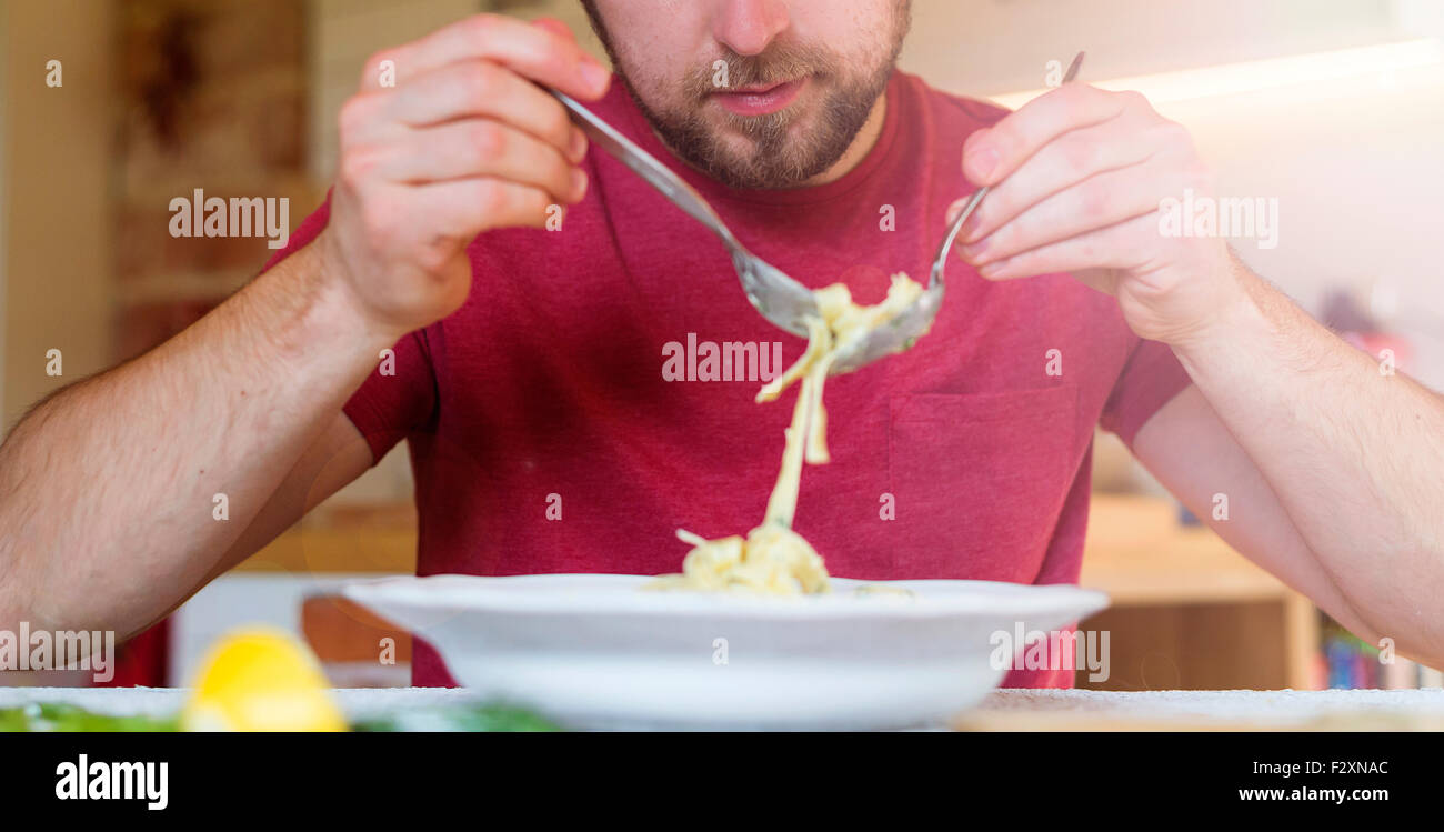 Young handsome man in the kitchen eating salmon tagliatelle Stock Photo