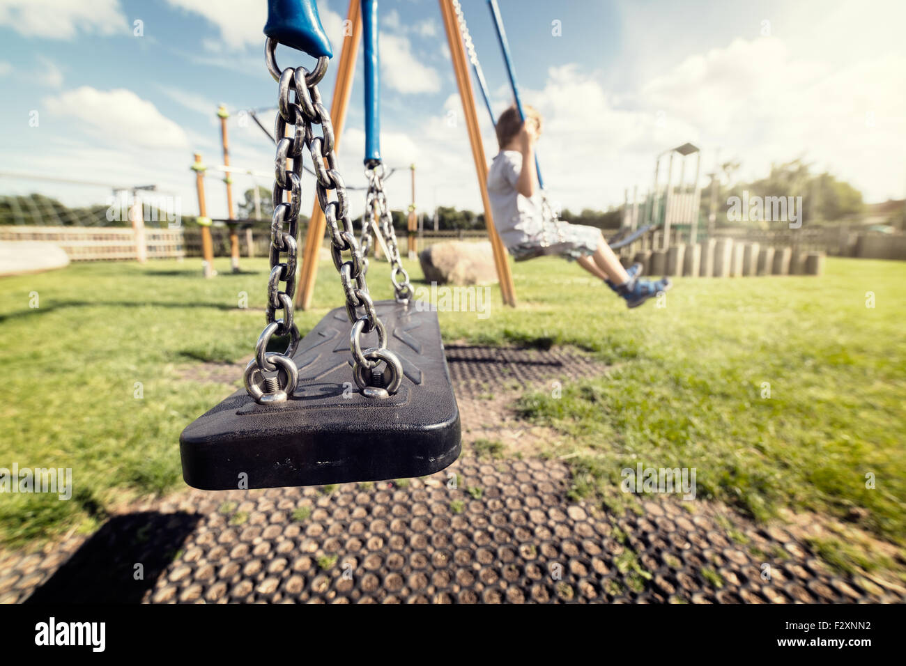 Empty playground swing with children playing in the background concept for child protection, abduction or loneliness Stock Photo