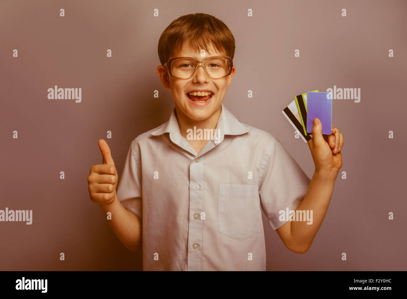 a boy of 10 years of European appearance with glasses holding kriditnye card in the hands of a thumbs up on a gray background re Stock Photo