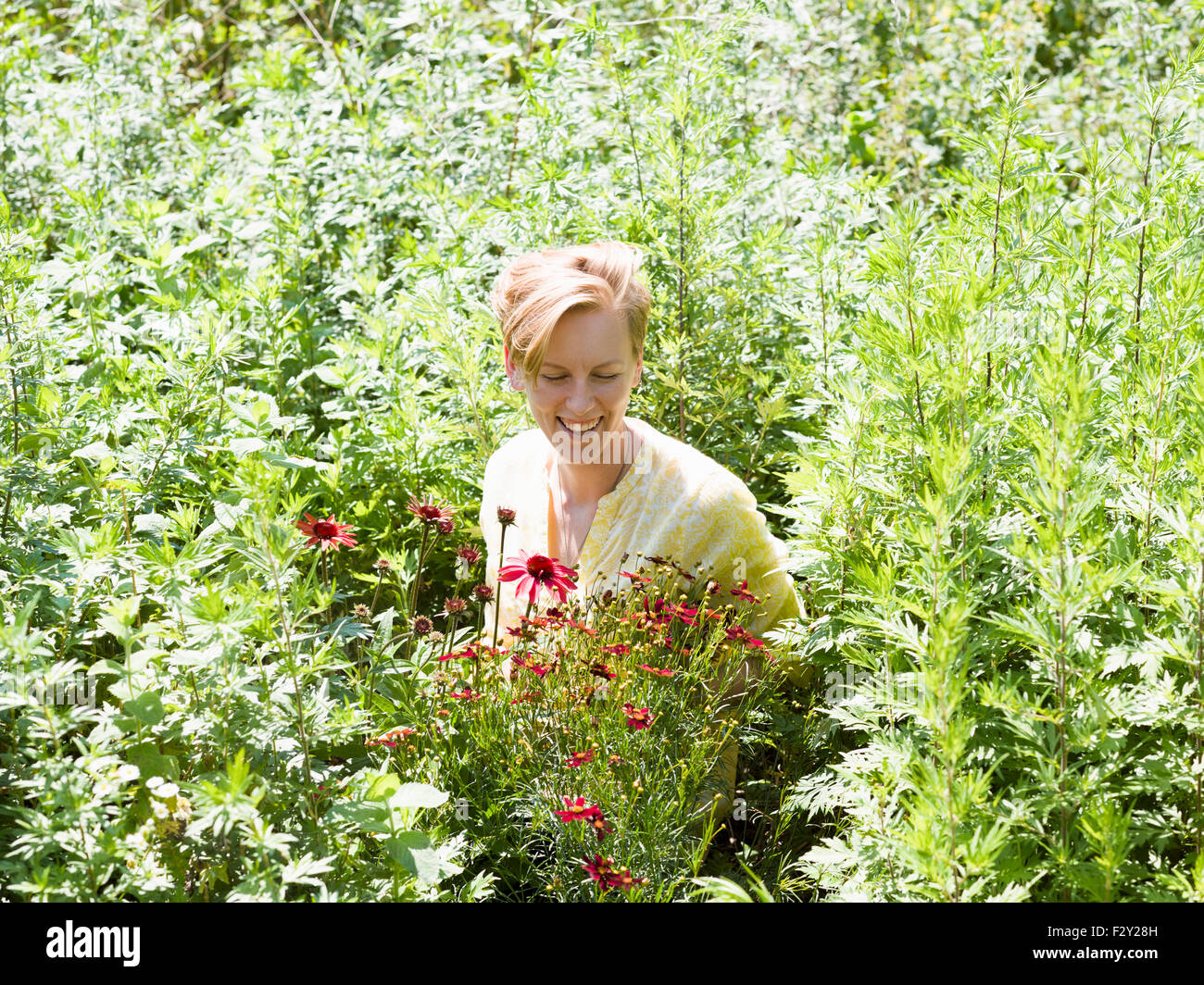 A young woman standing in a perennials bed surrounded by plants and flowers at a plant nursery. Stock Photo