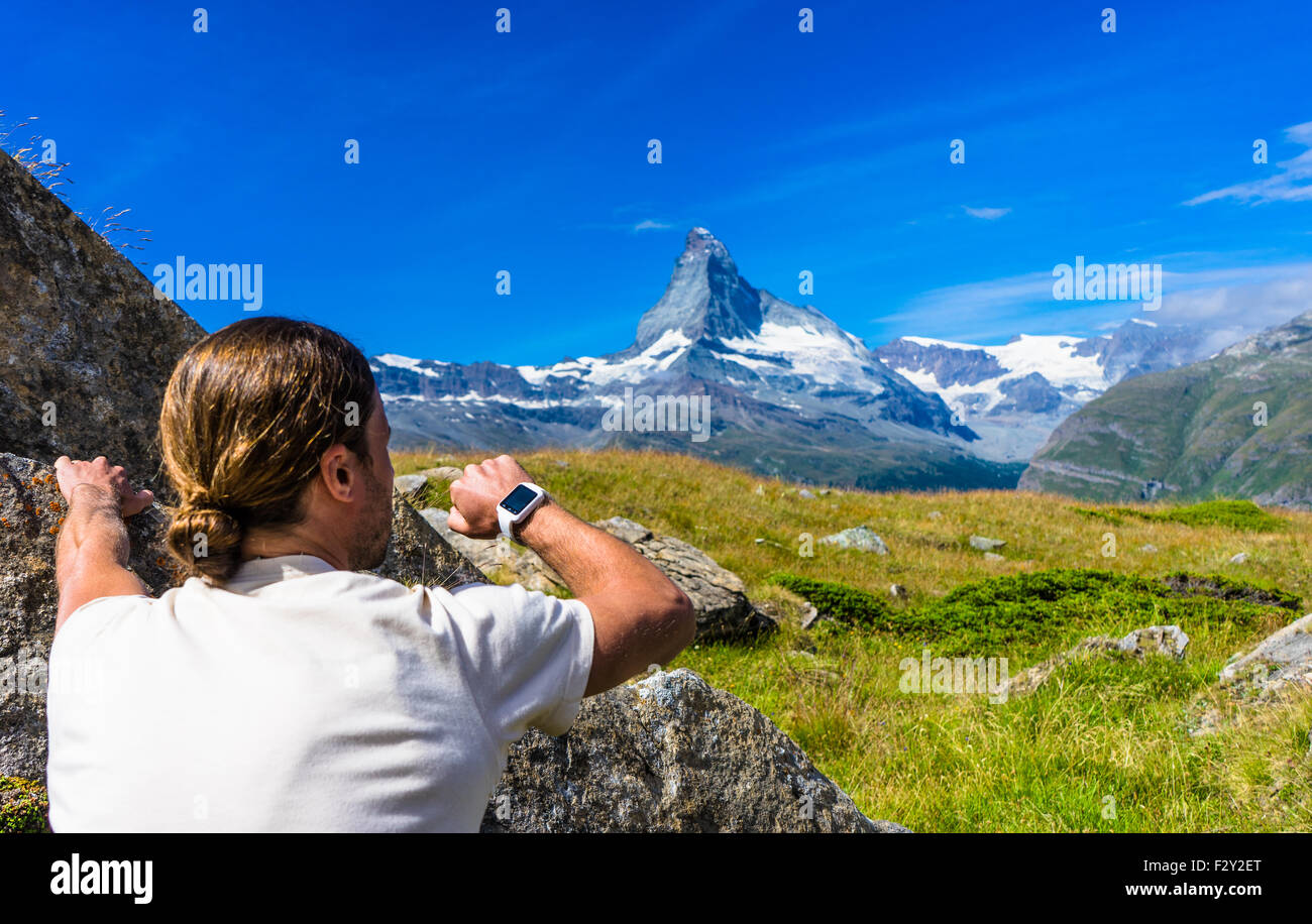 A rock climber checks his smart watch looking towards Matterhorn mountain, Switzerland. Stock Photo