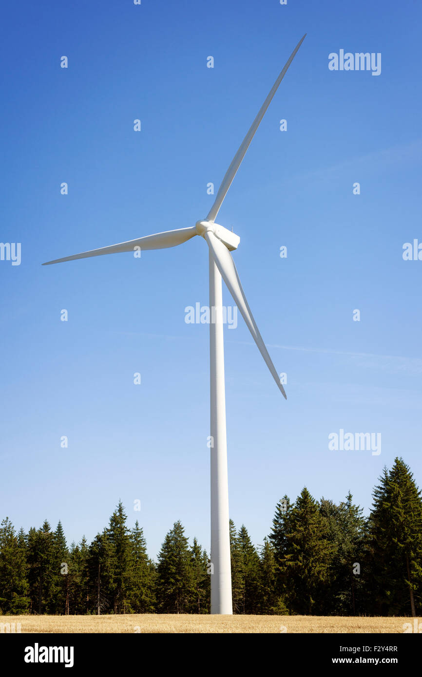 Wind turbine windfarm in field near trees with blue sky Stock Photo