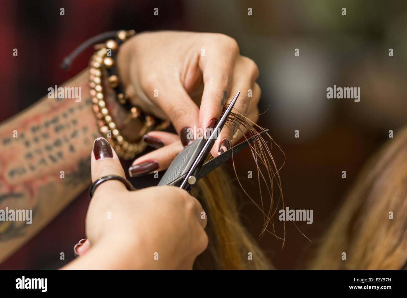 Closeup stylist hands with tattoo cutting brunette hair using scissors and  black coam Stock Photo - Alamy