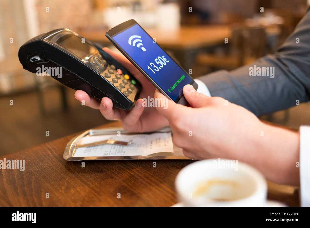 Man paying with NFC technology on mobile phone, in restaurant, bar, cafe. Euro French version Stock Photo