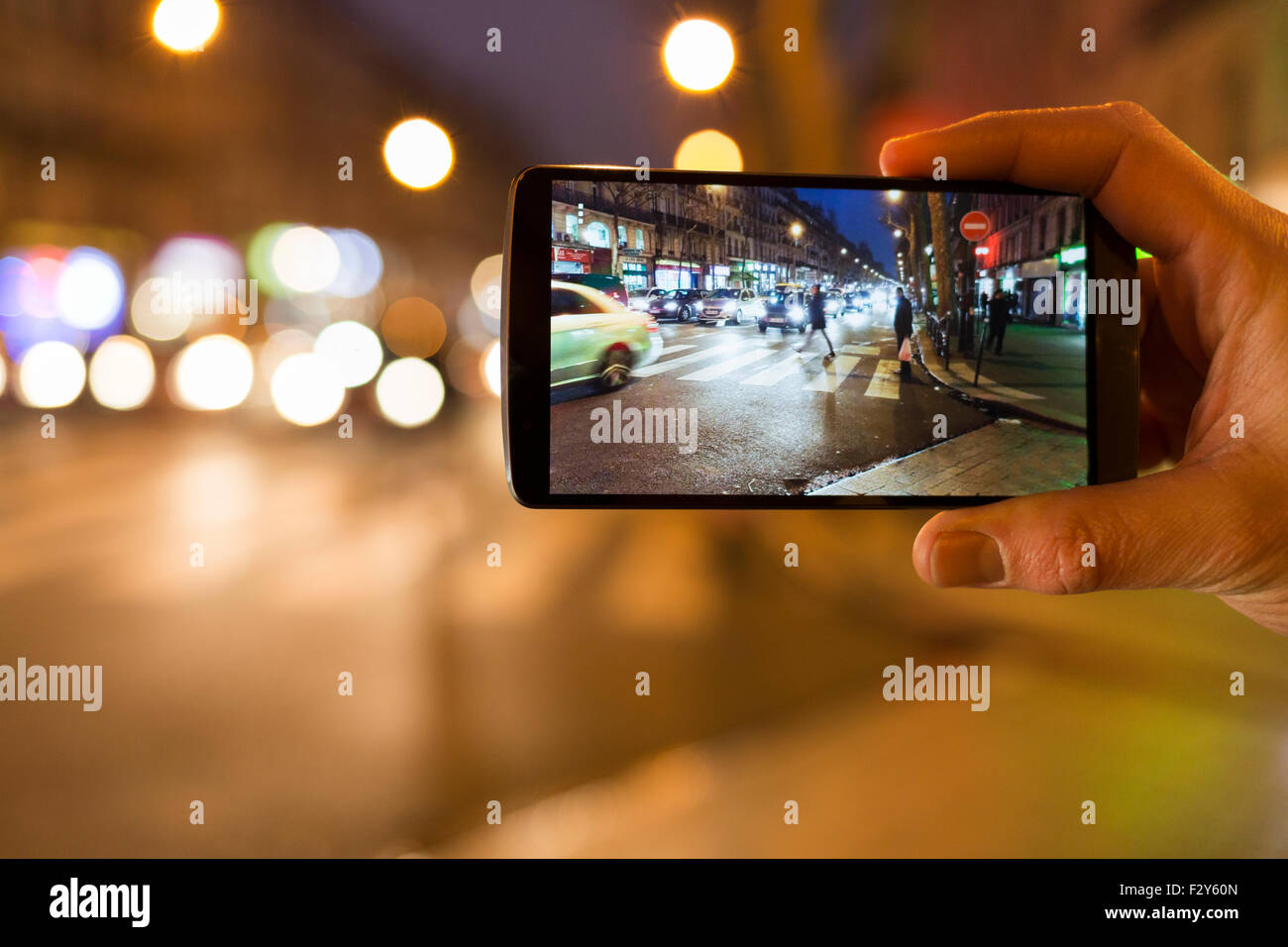 Man makes a picture in the street with his mobile phone. Night light bokeh background Stock Photo